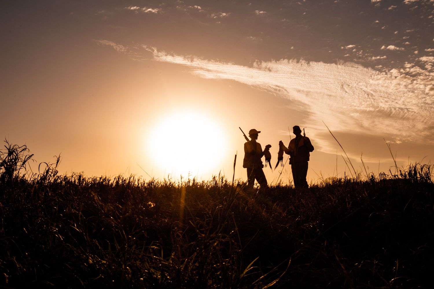 Silhouettes of hunters walking along a ridge at sunset.