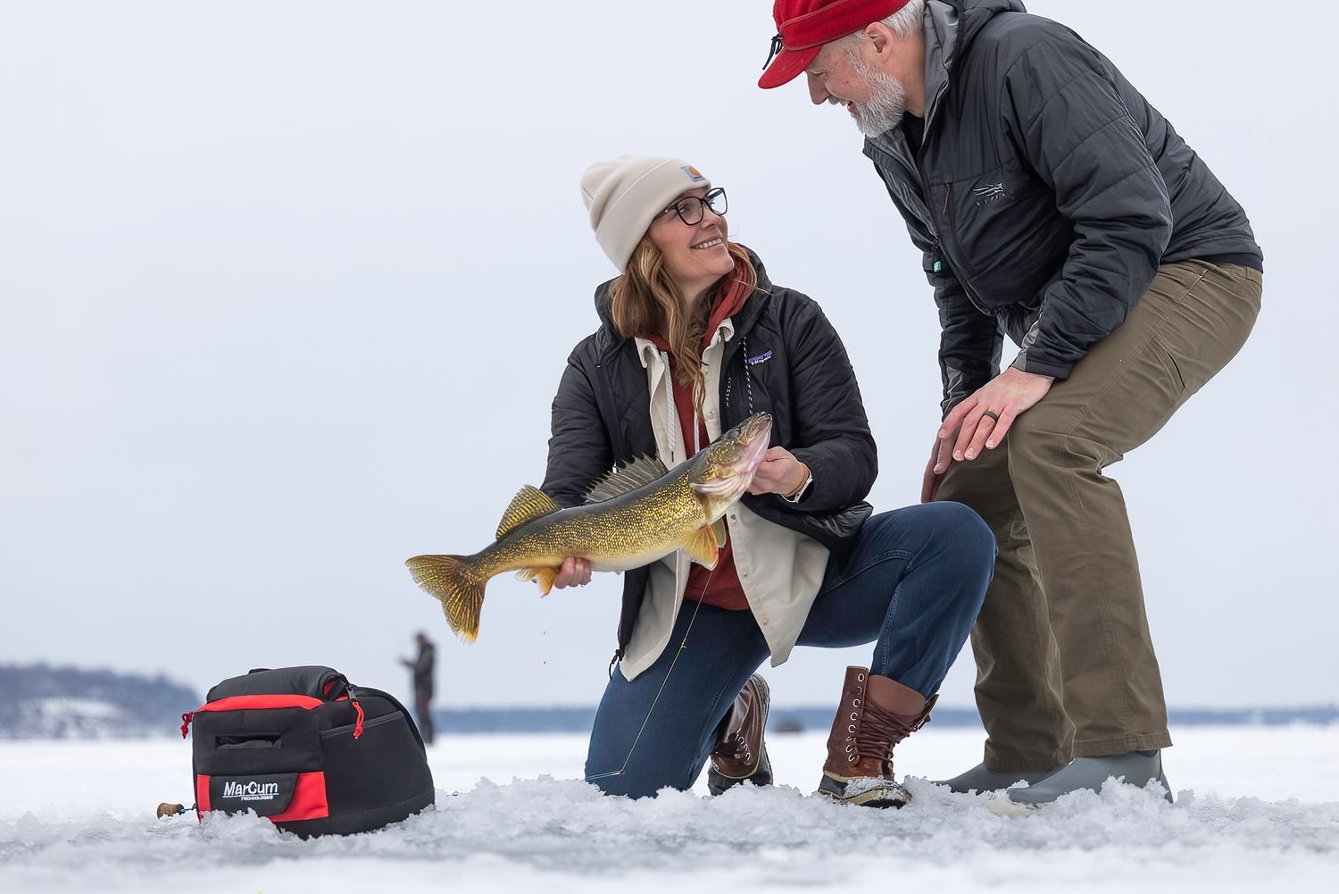 Anglers kneeling in the snow while ice fishing on a frozen lake.