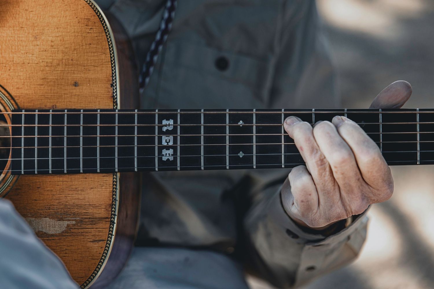 Detailed shot of fingers playing wooden acoustic guitar with natural shadow patterns.