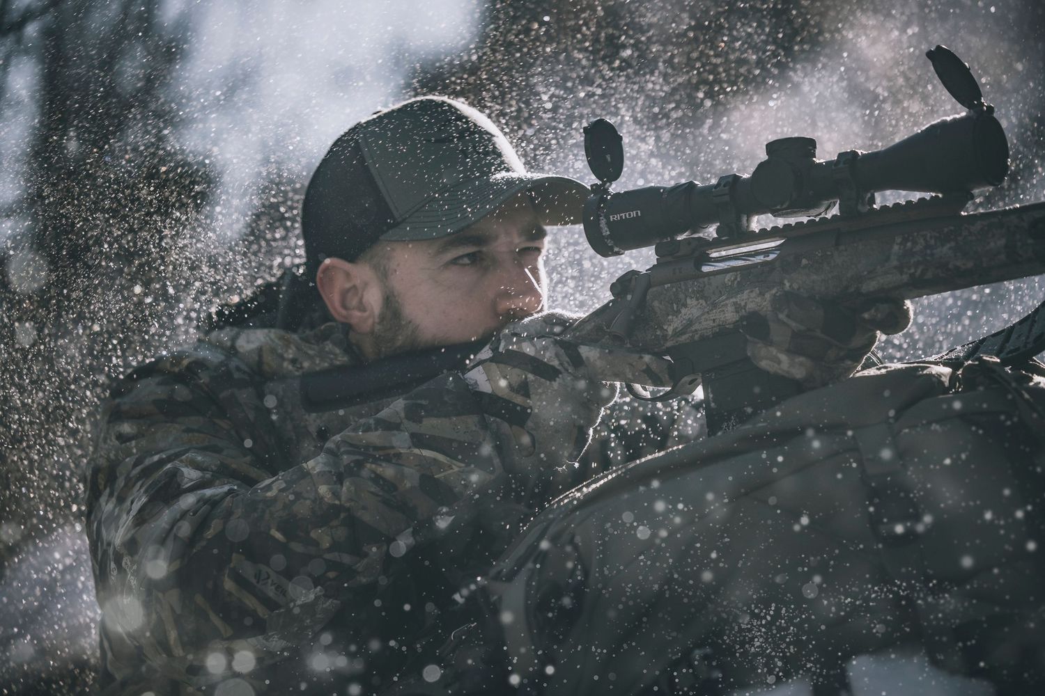 A hunter aims a scoped rifle in snowy winter conditions.