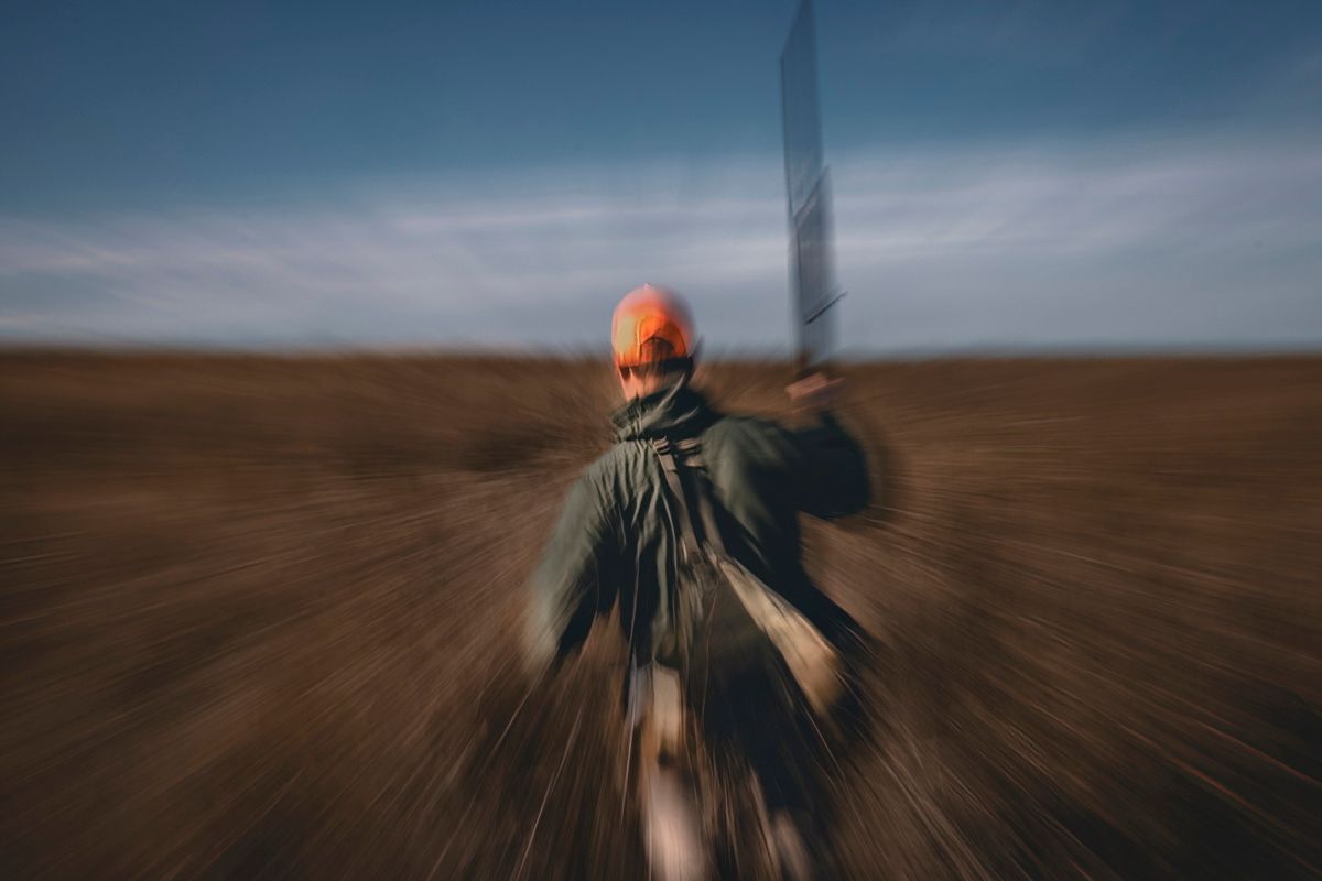 Blurred motion shot of hunter in orange safety gear walking through field.
