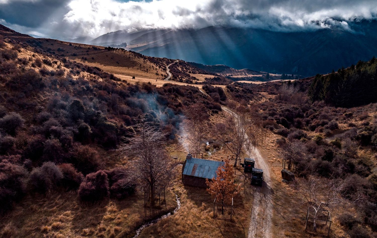 Aerial view of small cabin nestled in rugged mountain terrain under dramatic sky.