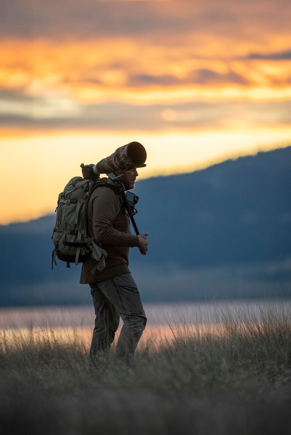 Silhouette of a photographer with backpack standing in a field at sunset.