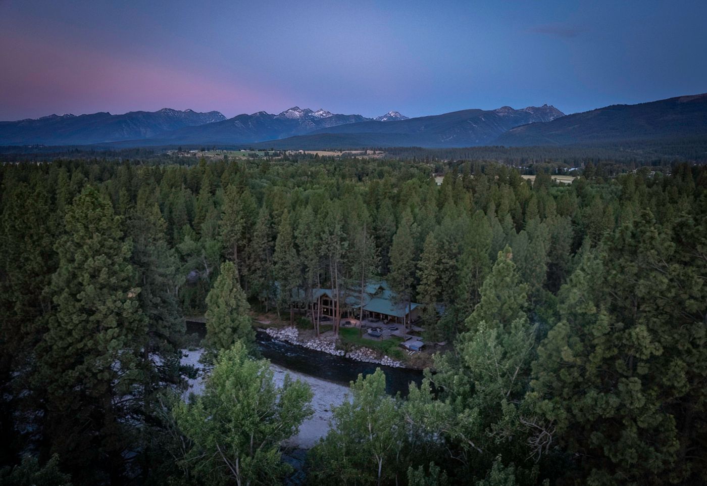 Panoramic mountain landscape with forest and river winding through valley at dusk.