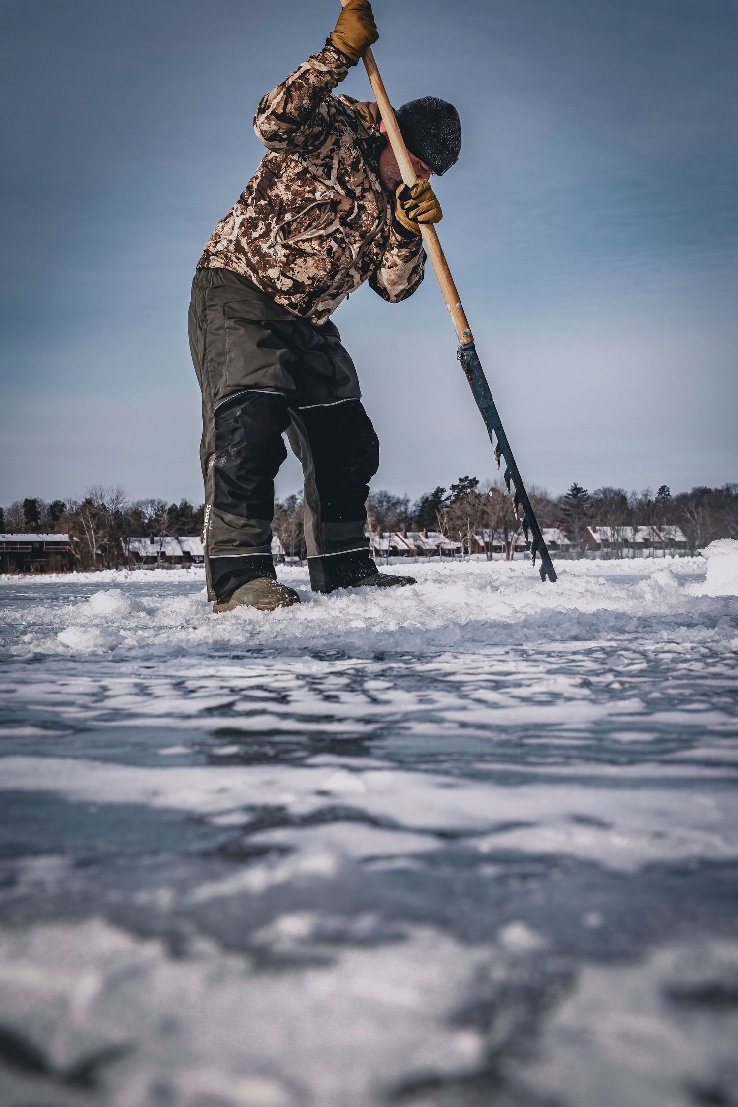 Ice fisher cutting hole in frozen lake wearing camouflage gear.