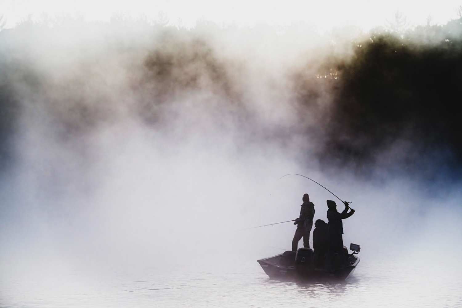 Misty silhouette of people fishing from a small boat on foggy waters.