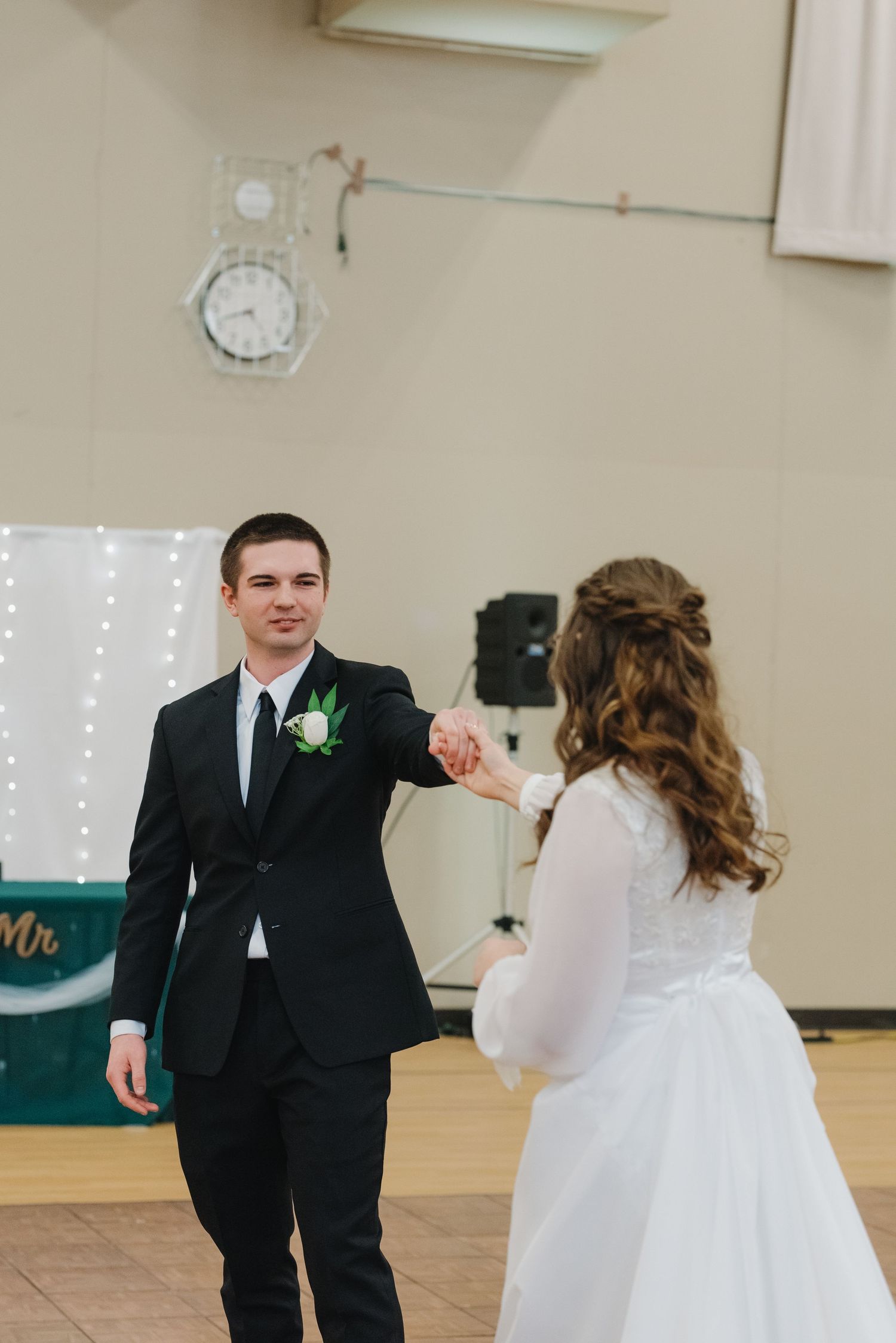Bride and groom sharing their first dance, holding hands on a wooden dance floor at wedding reception.