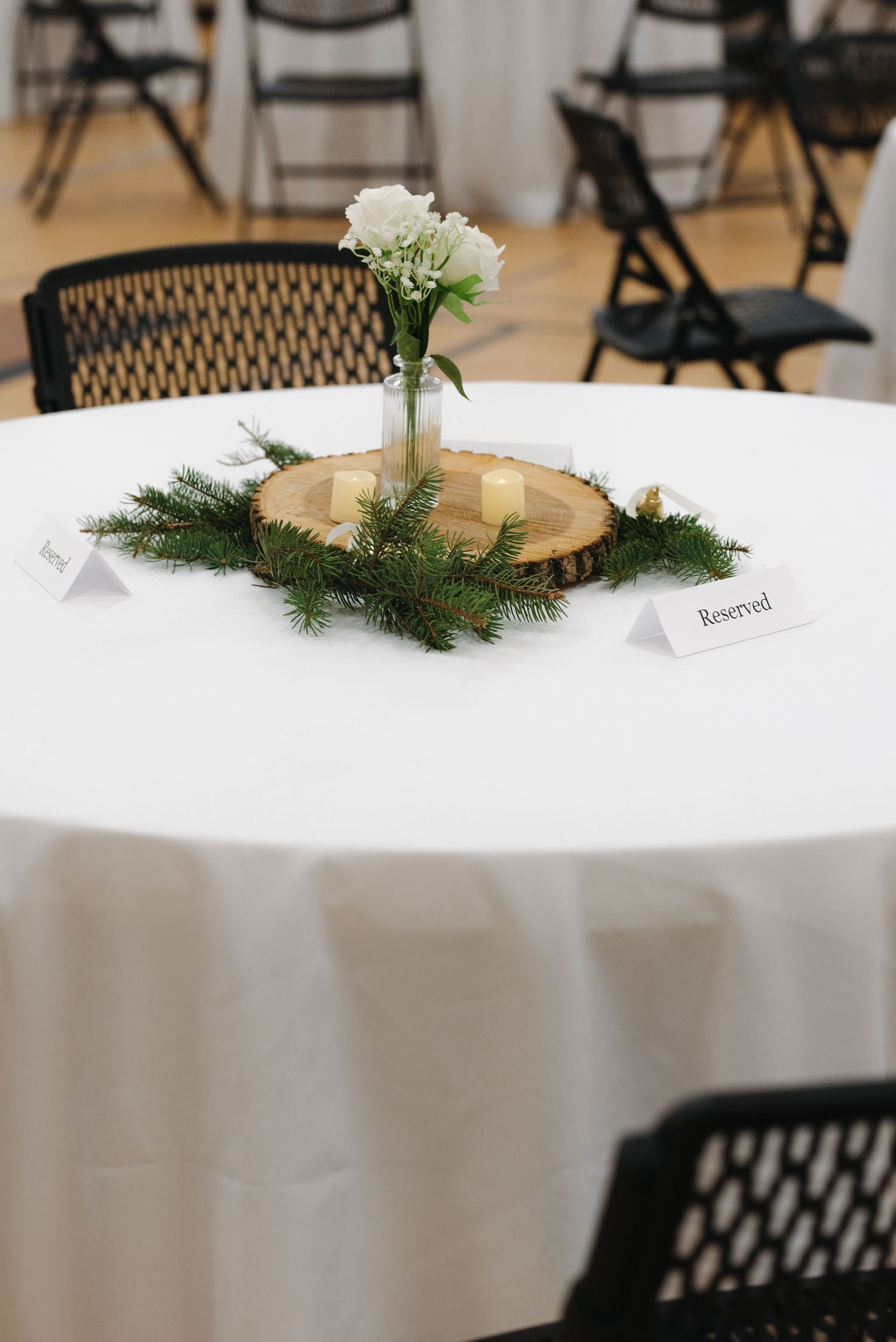 Elegant wedding reception table with white linen, wood slice centerpiece, greenery, and reserved cards.