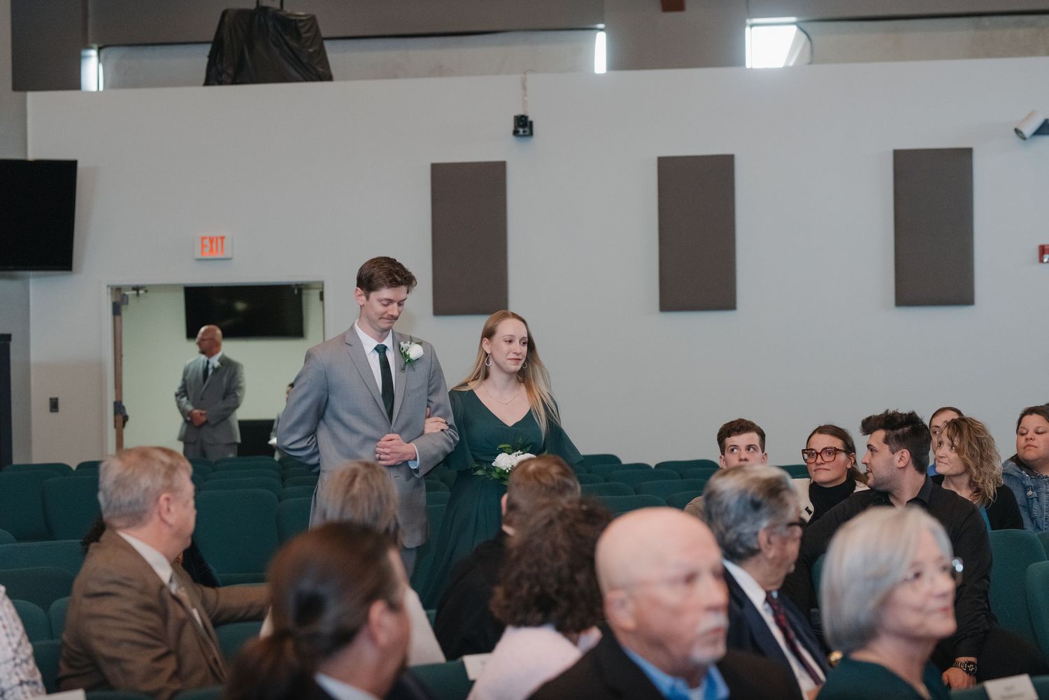 A couple in formal attire walks down the aisle at a wedding ceremony in a modern church venue.