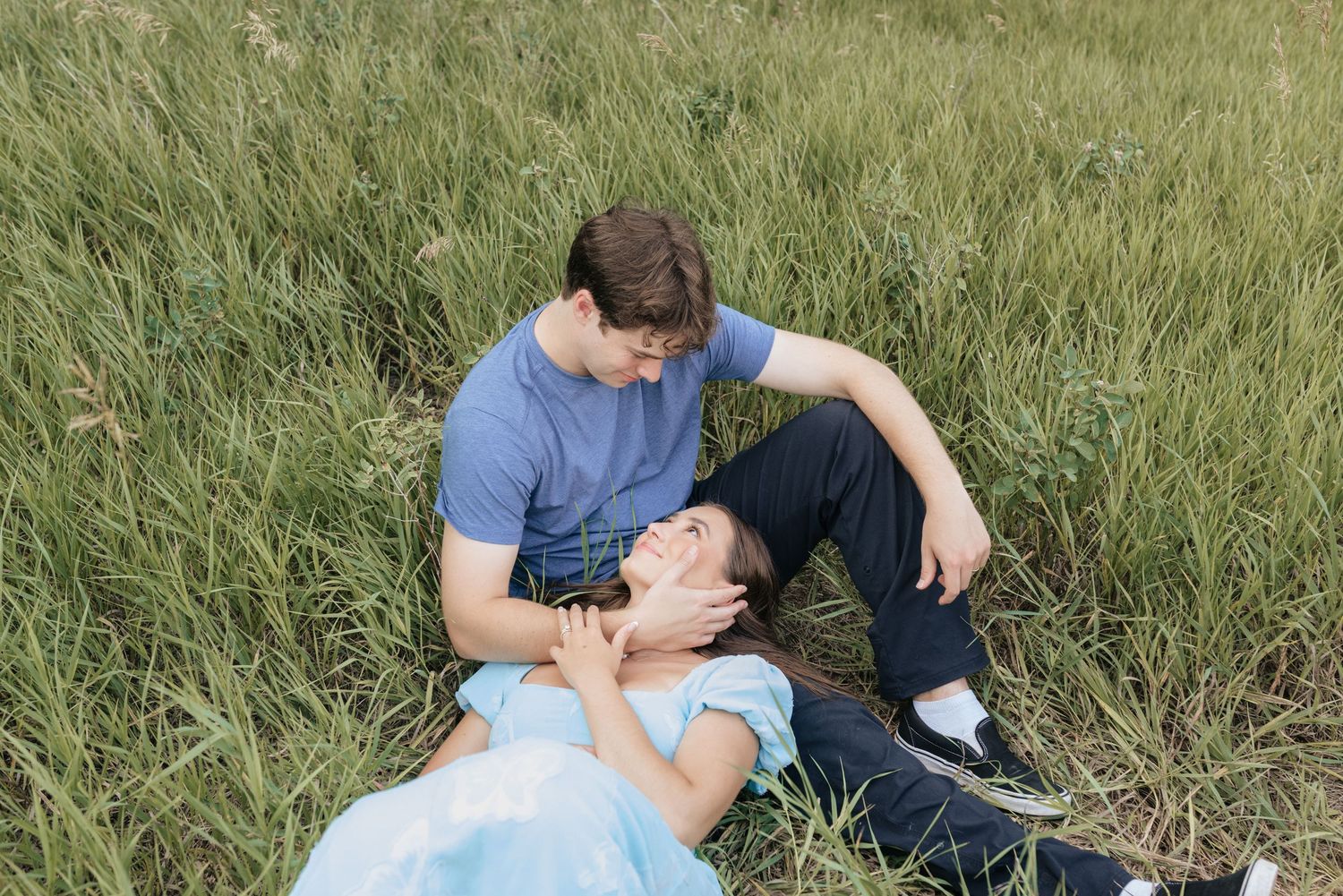 Couple sitting in a lush green field, woman resting her head on man's lap, sharing a tender moment.