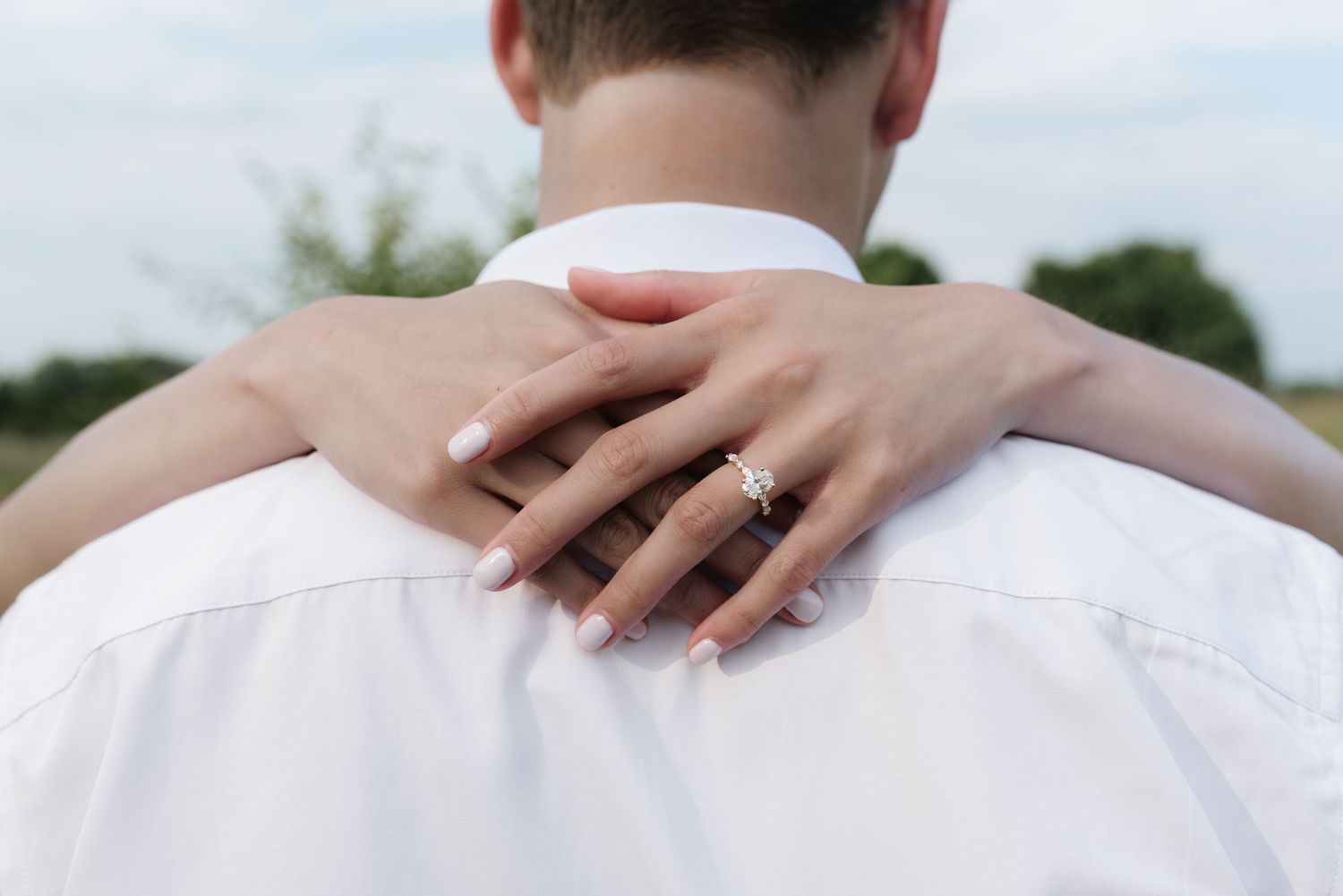 Close-up of womans hand with diamond engagement ring resting on mans white shirt back.