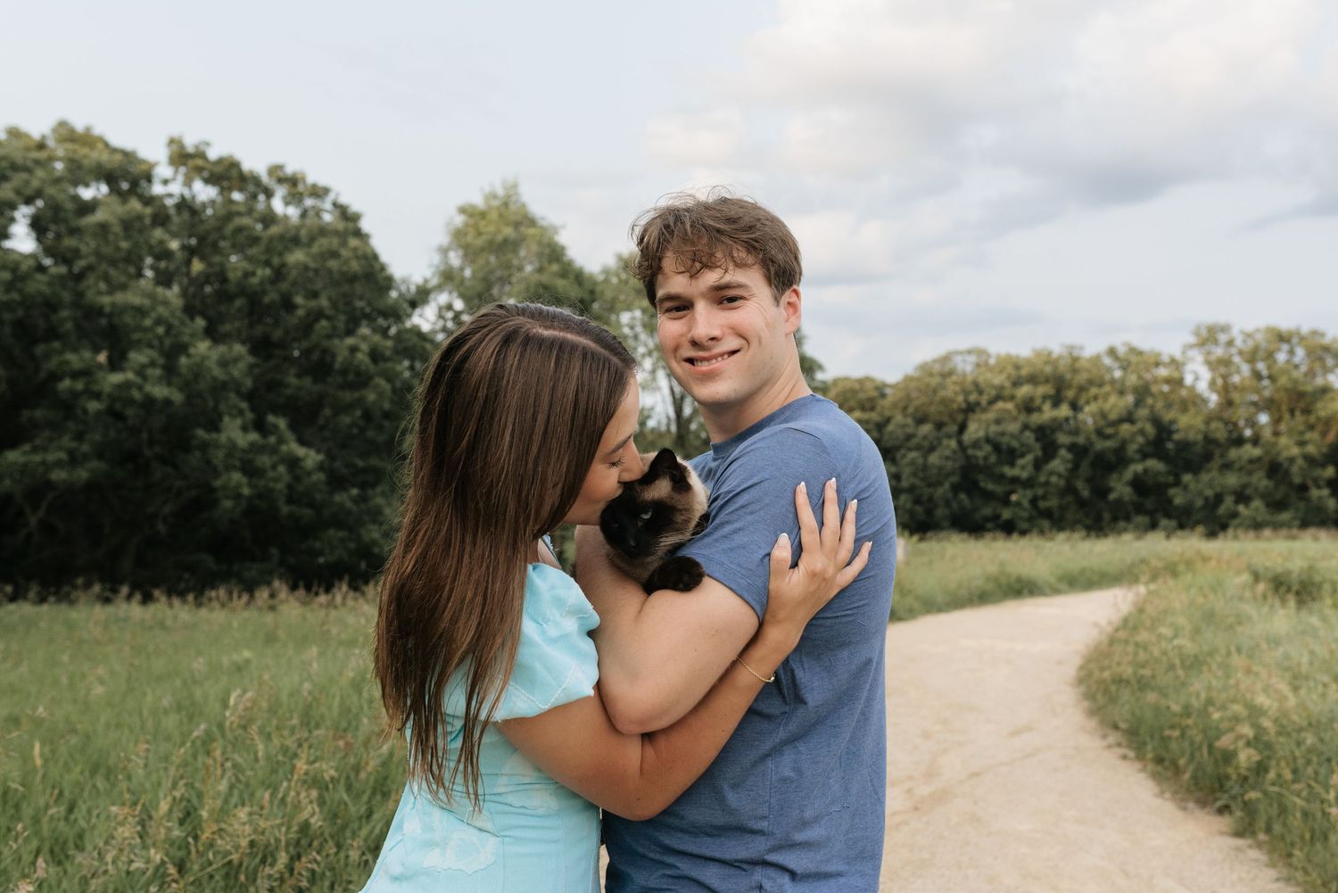 Happy couple holding a small cat outdoors in a green field on a sunny day.