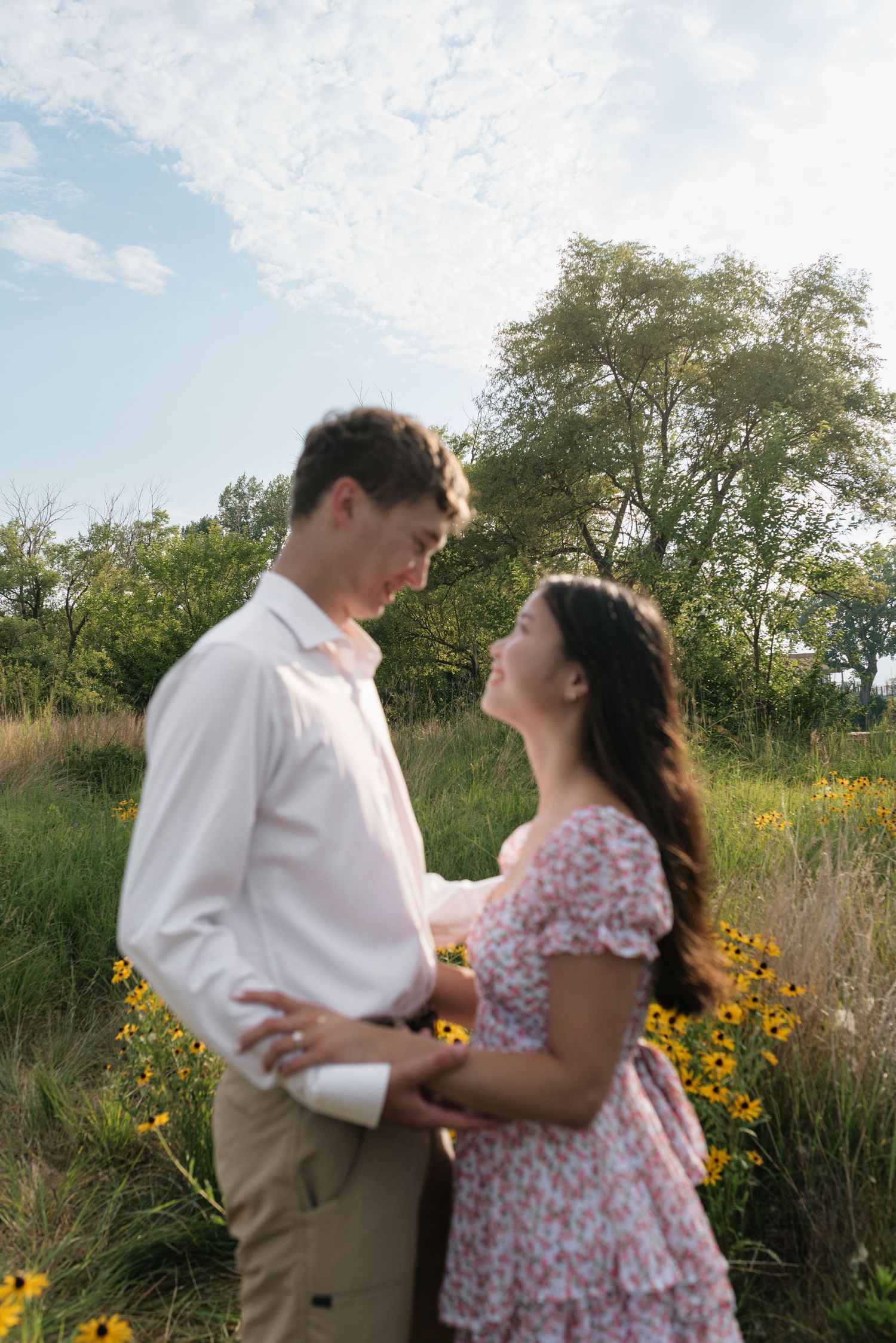 Romantic couple holding hands and looking at each other in a golden hour meadow setting.