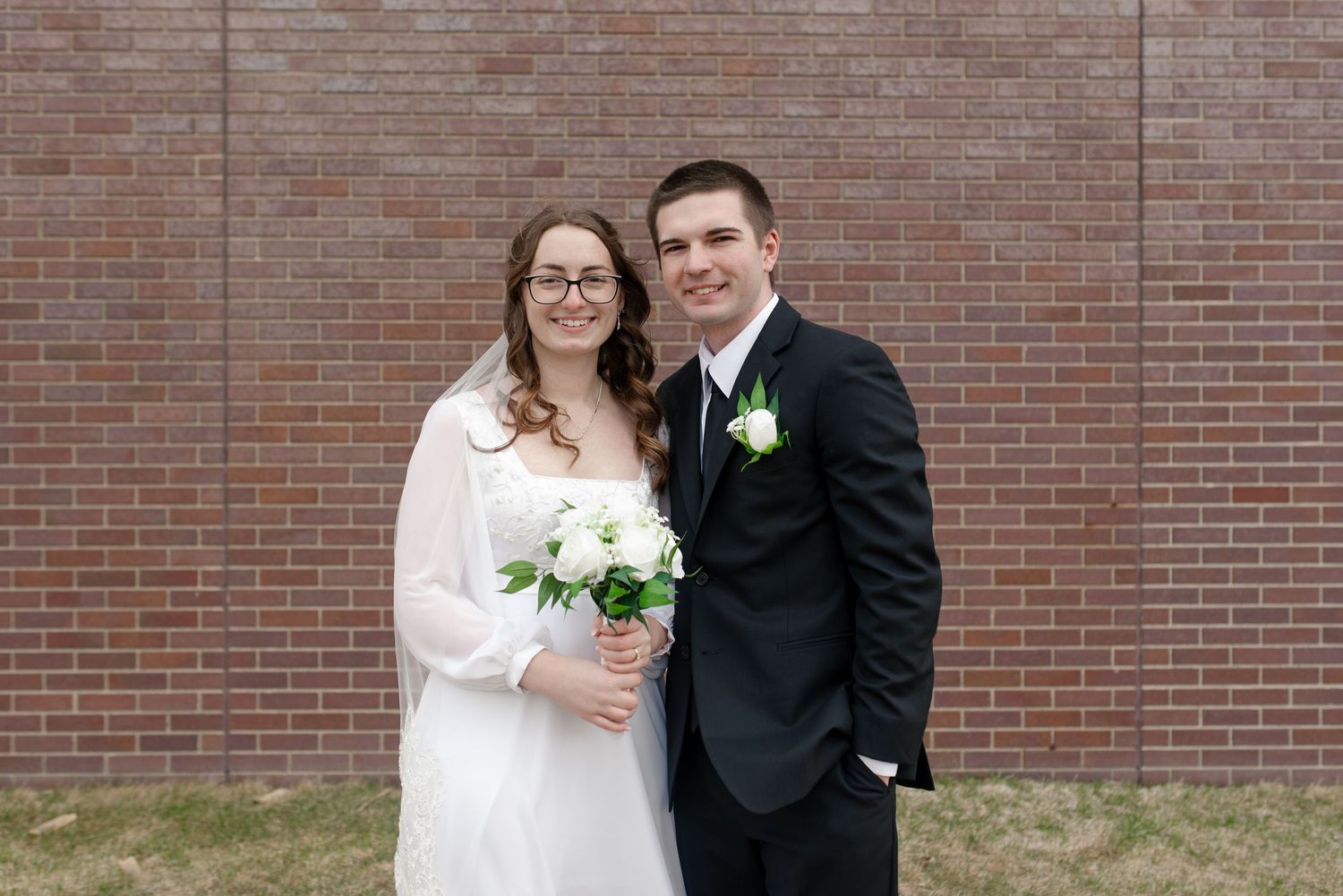 Happy bride and groom standing together in front of brick wall on their wedding day.