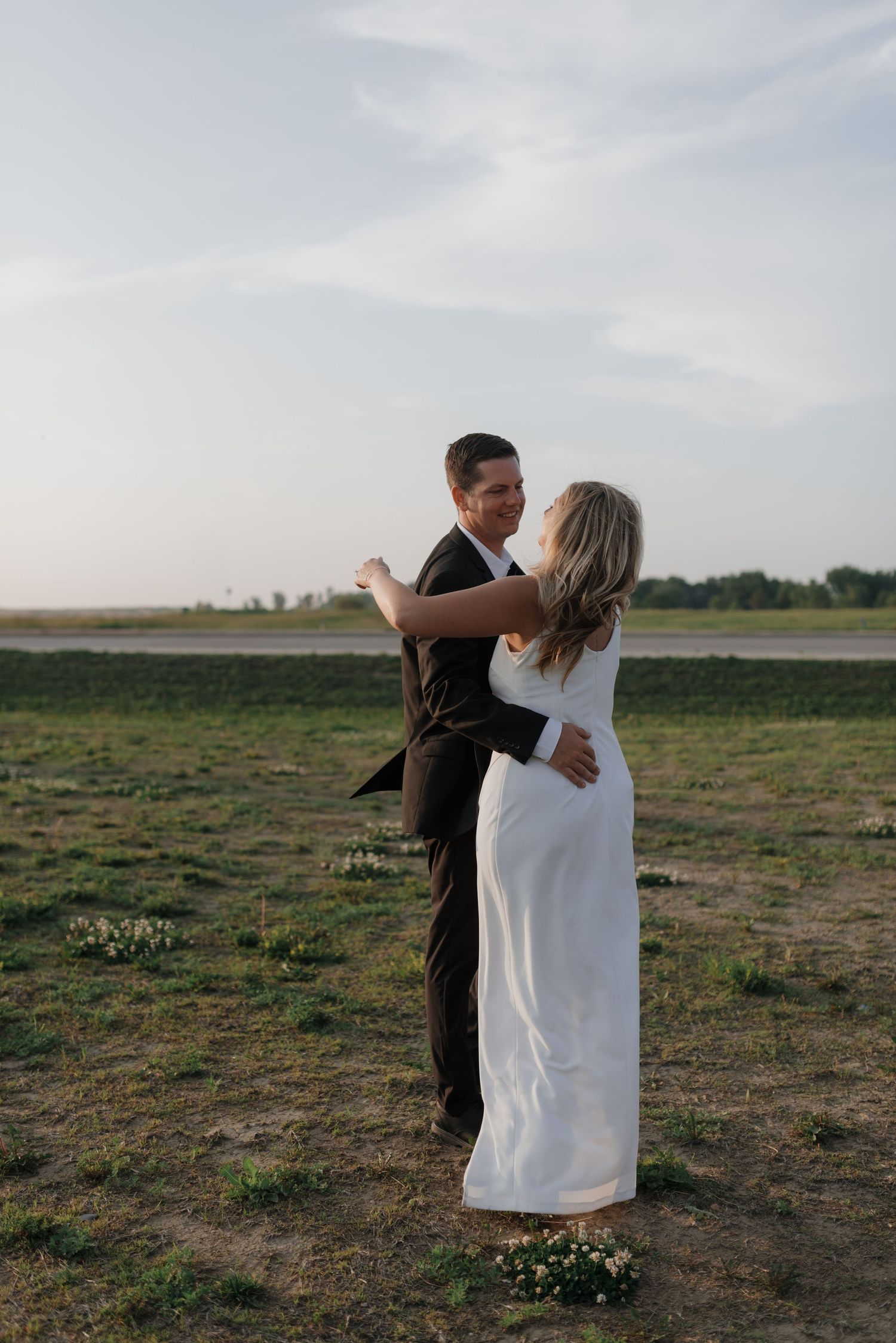 Bride and groom dance together in open green field during outdoor wedding photo session.