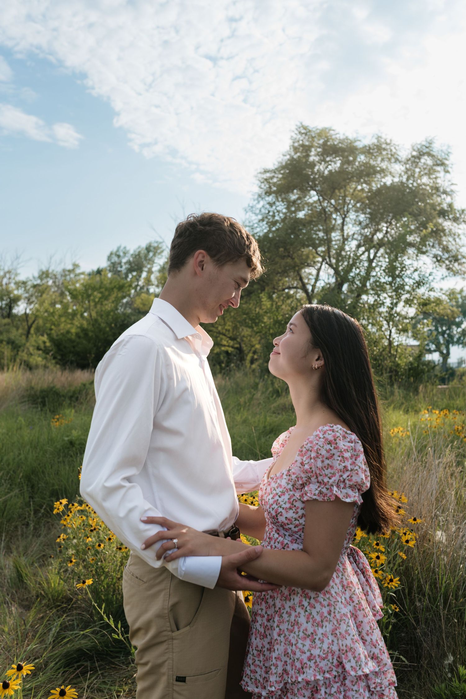 Couple gazing at each other surrounded by yellow wildflowers in a sunny green meadow.