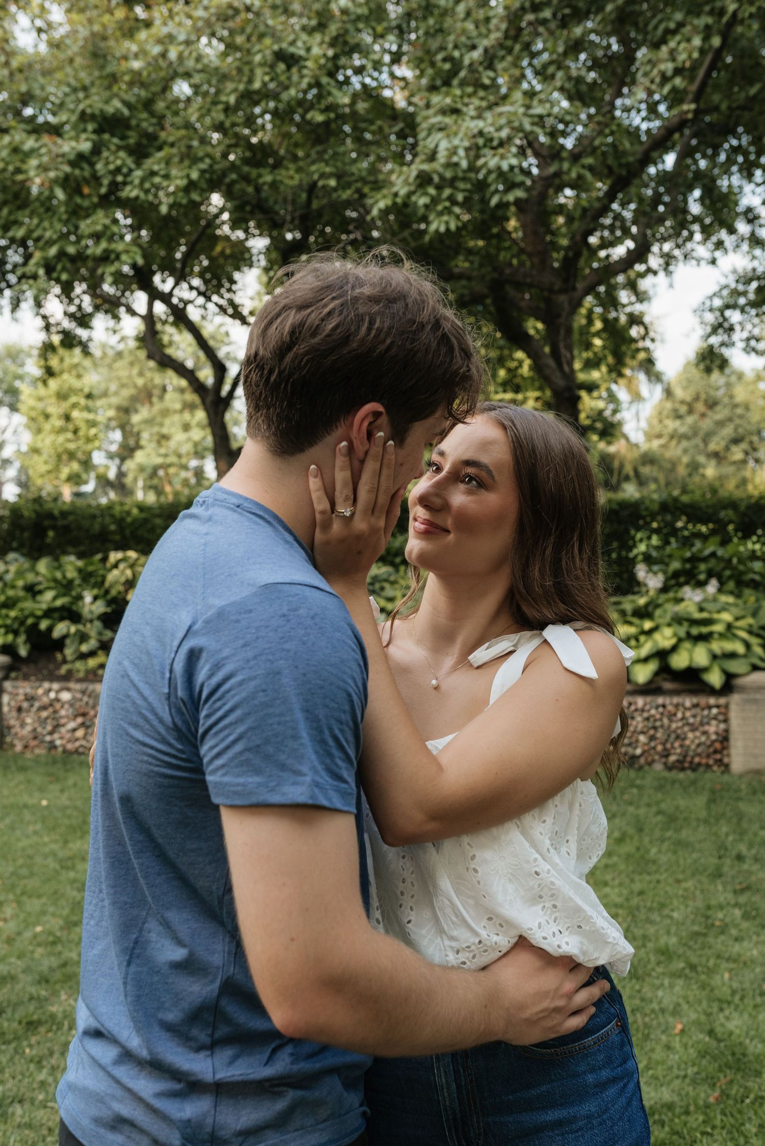 A couple shares a romantic moment outdoors, the woman smiling as they embrace in a lush garden setting.