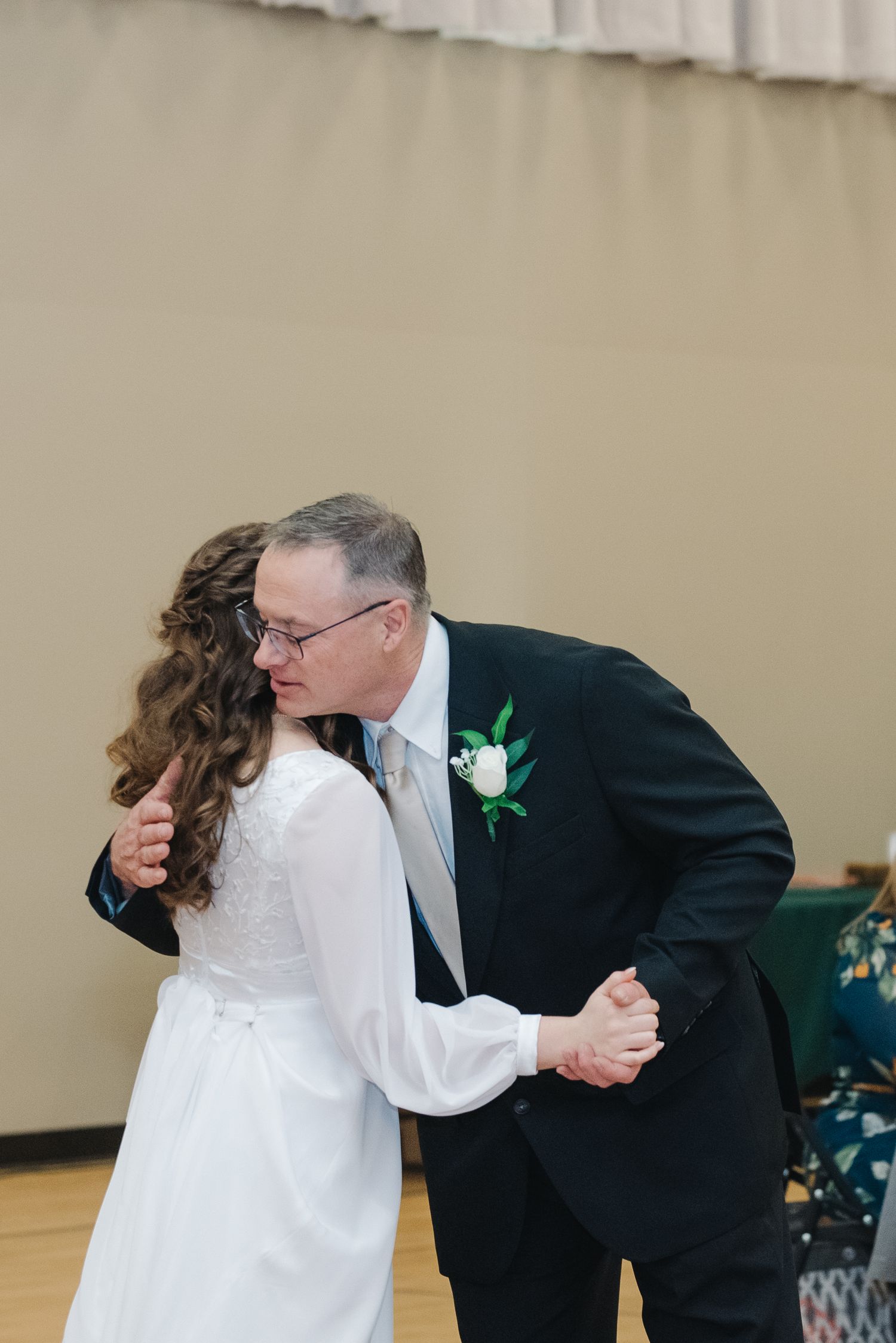 Bride sharing an emotional father-daughter dance with older man in black suit at wedding reception.