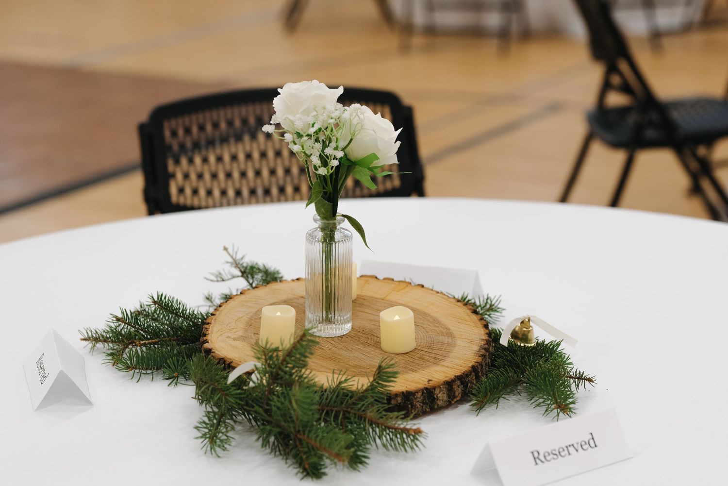 Elegant rustic wedding centerpiece with white flowers, candles, and greenery on a wood slice.