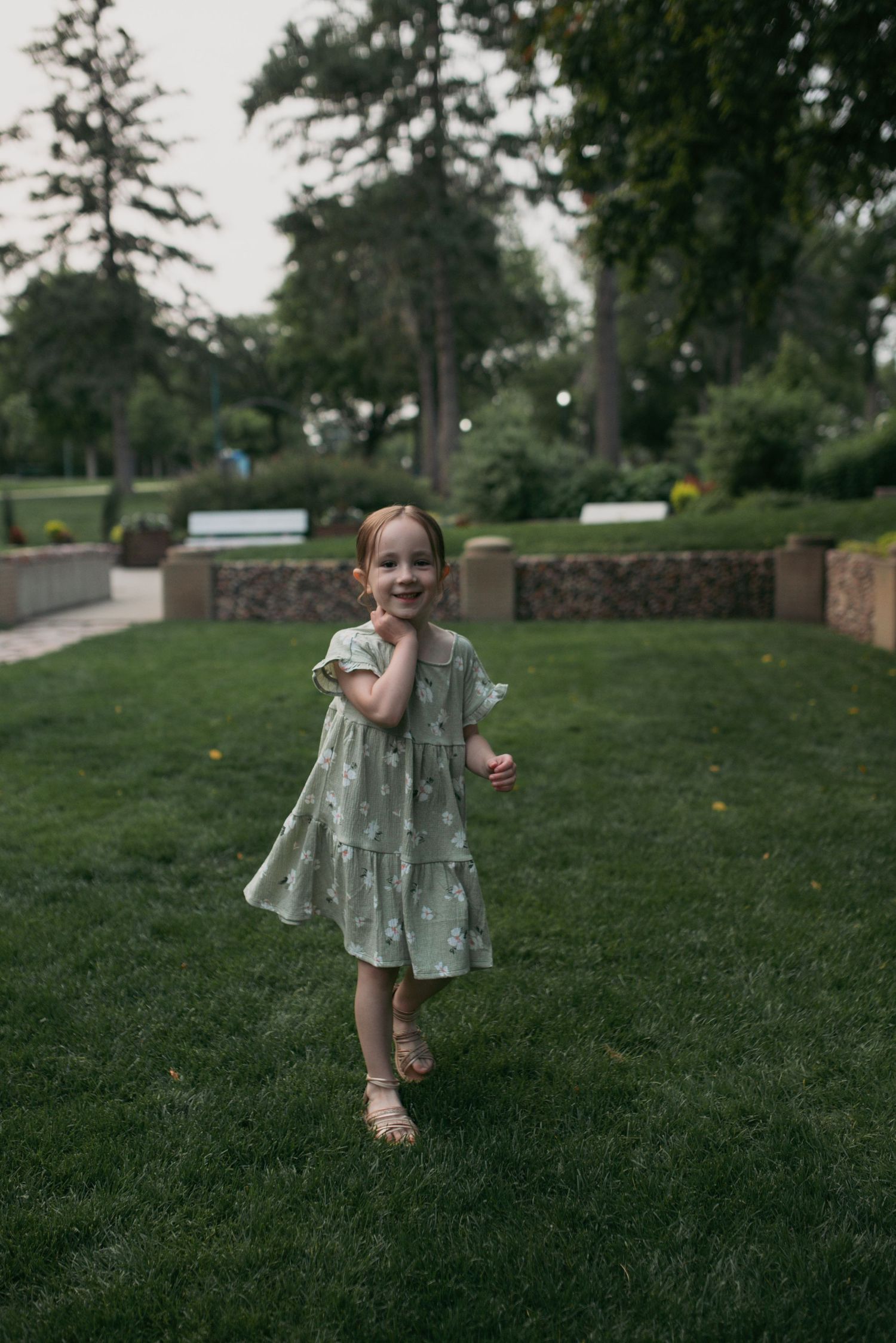 Happy little girl in green floral dress running and smiling on grass in a park.
