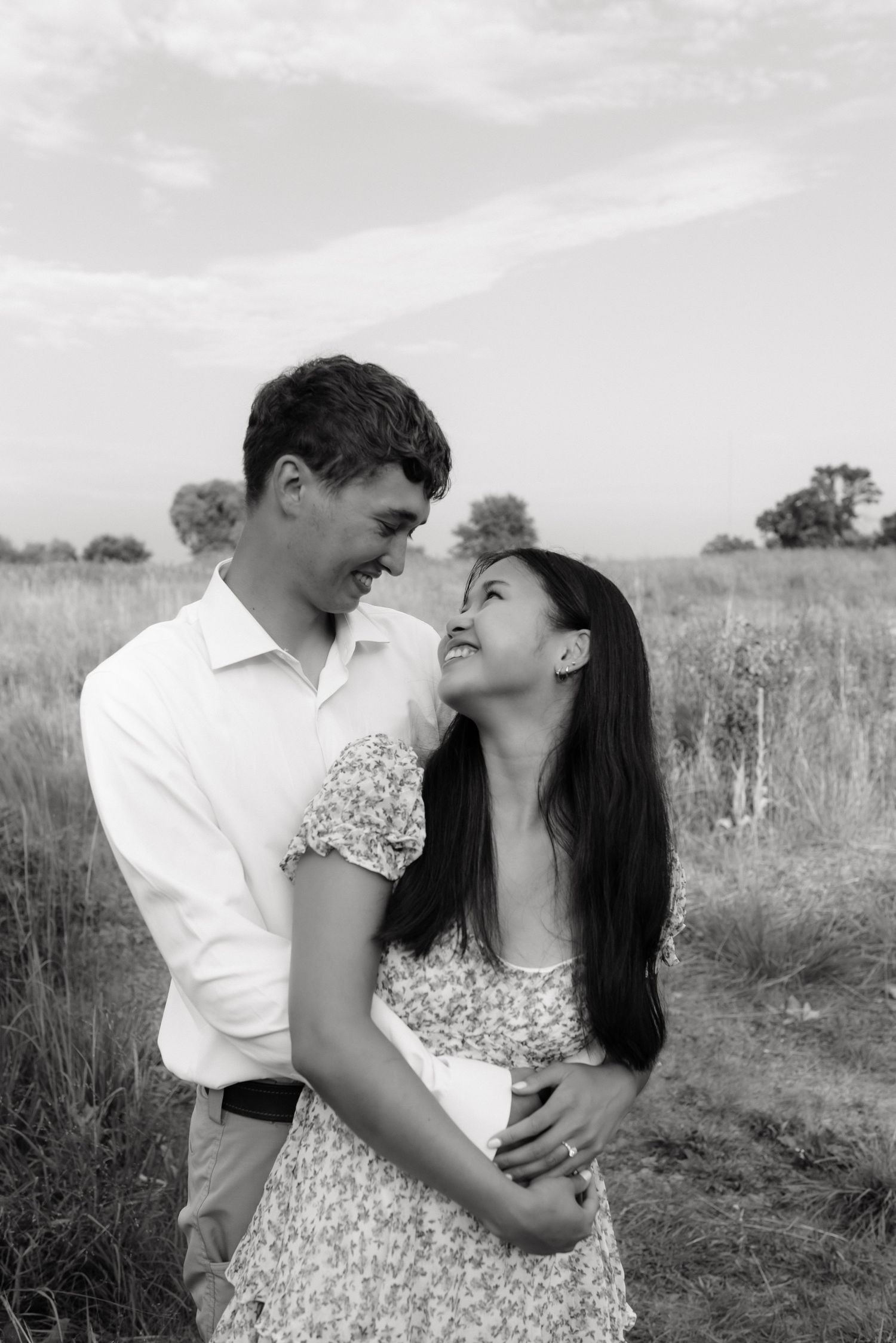 Black and white photo of a laughing couple embracing closely in an open field.