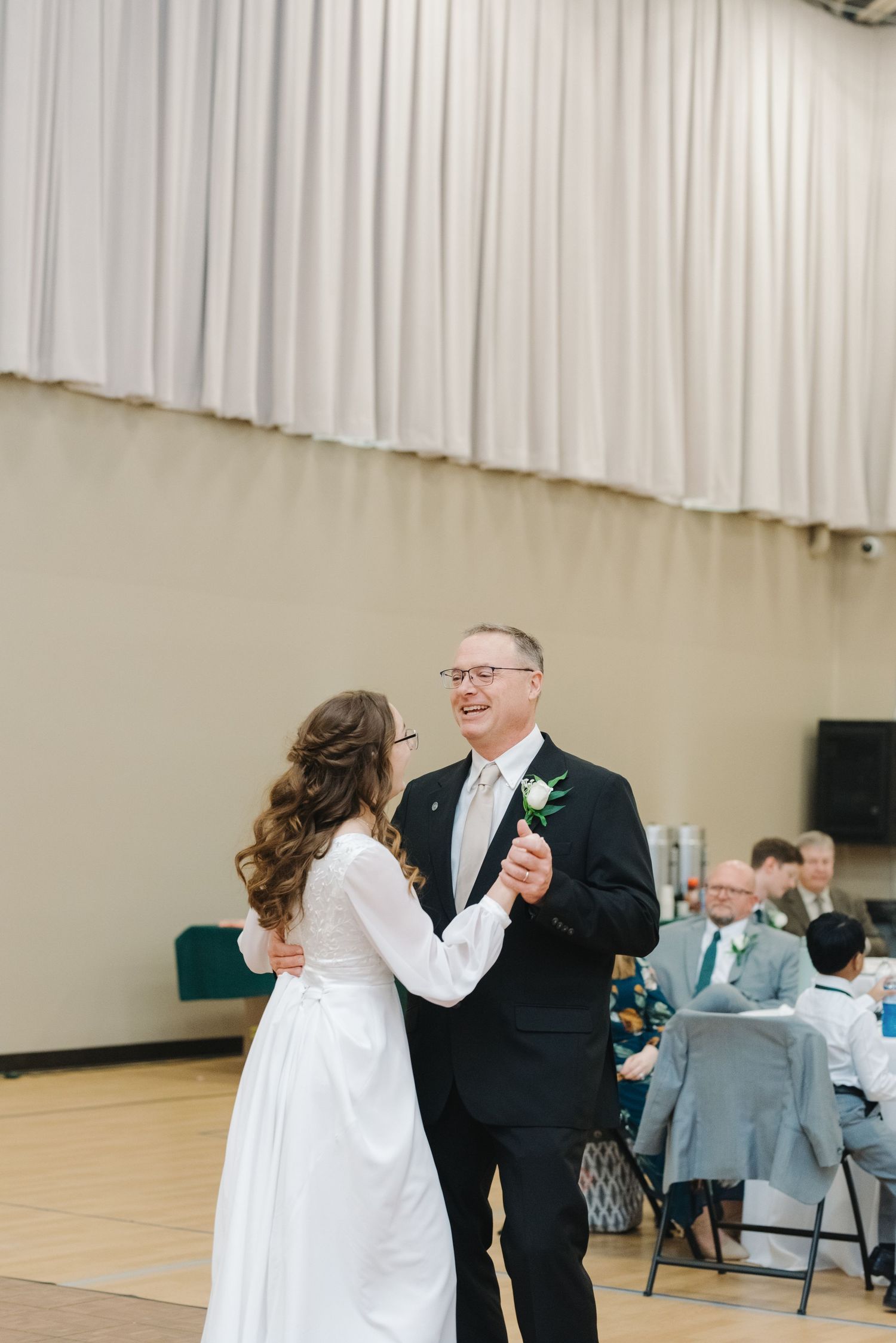 Bride and father sharing joyful first dance at wedding reception in elegant white gown.