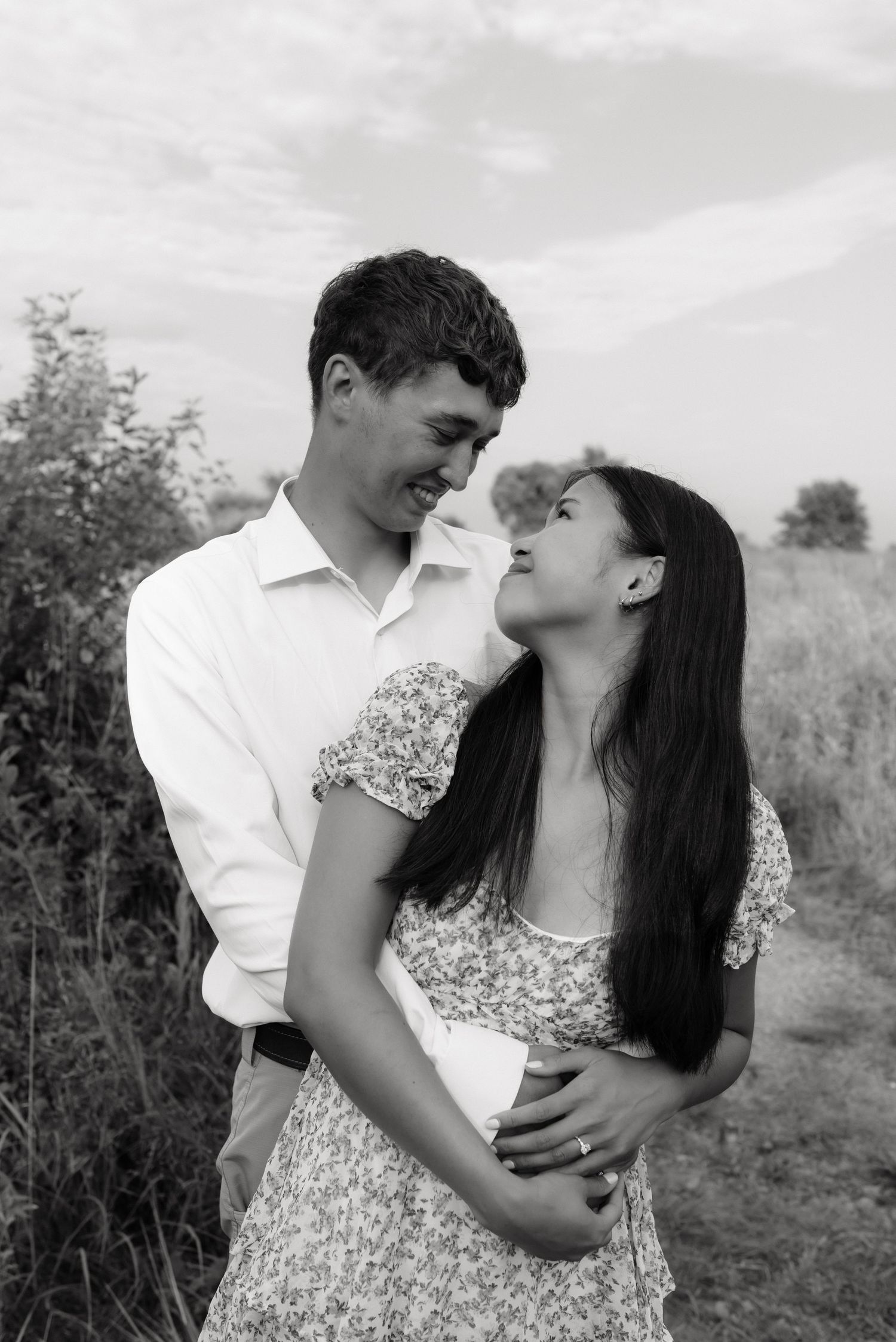 Black and white portrait of a smiling couple embracing outdoors in a natural setting.