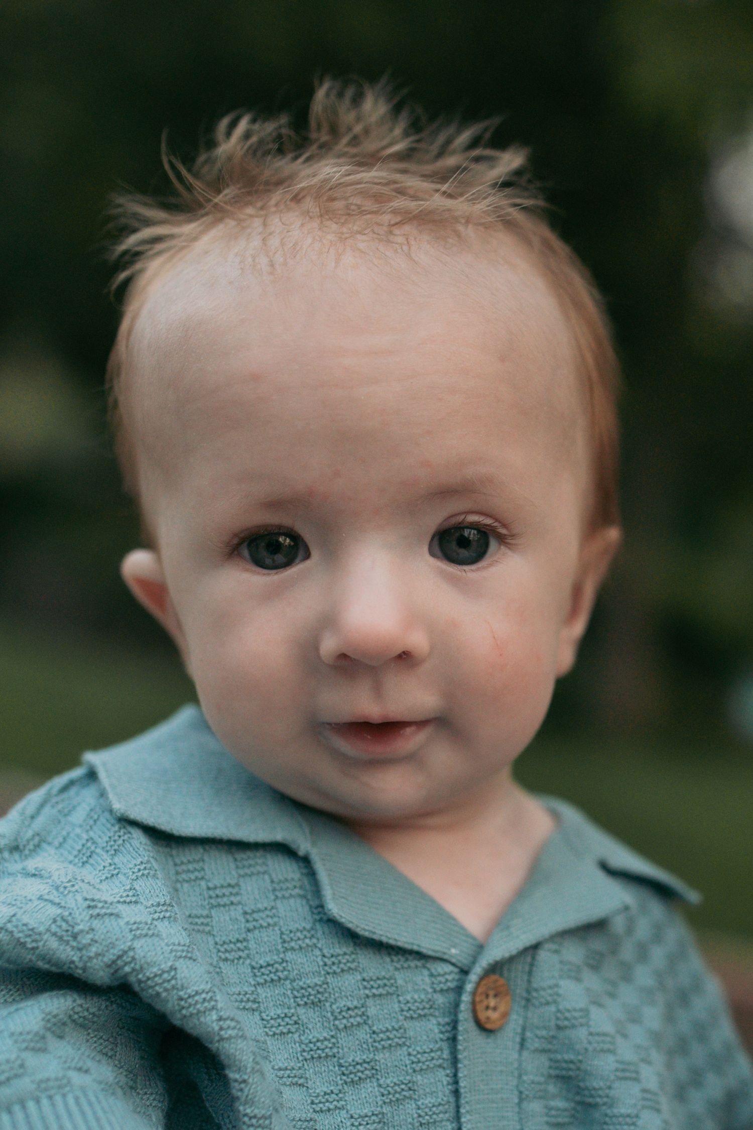 Close-up portrait of an adorable baby with blue eyes wearing a teal knit collared outfit.