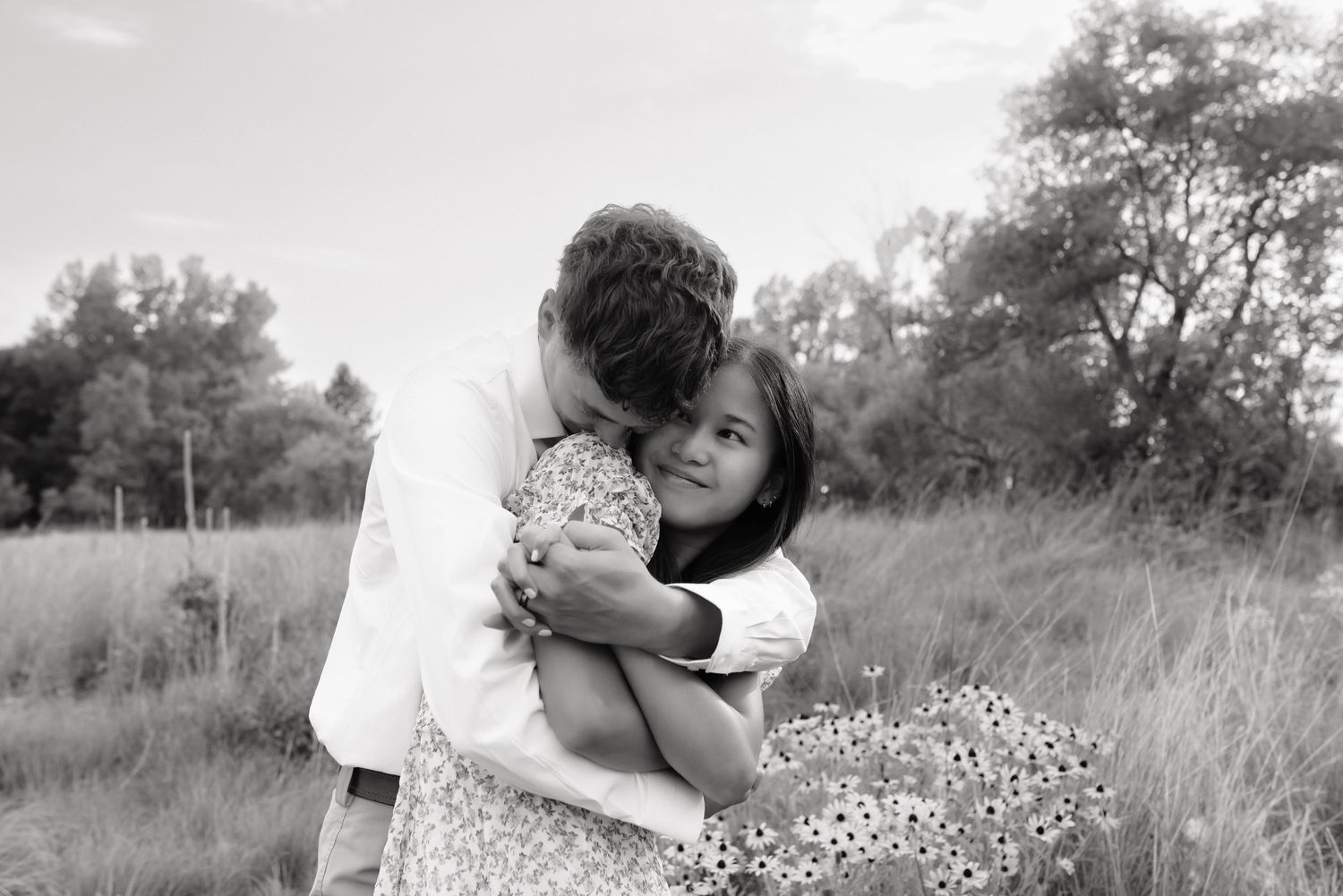 Black and white photo of couple embracing in meadow, man kissing womans cheek tenderly.