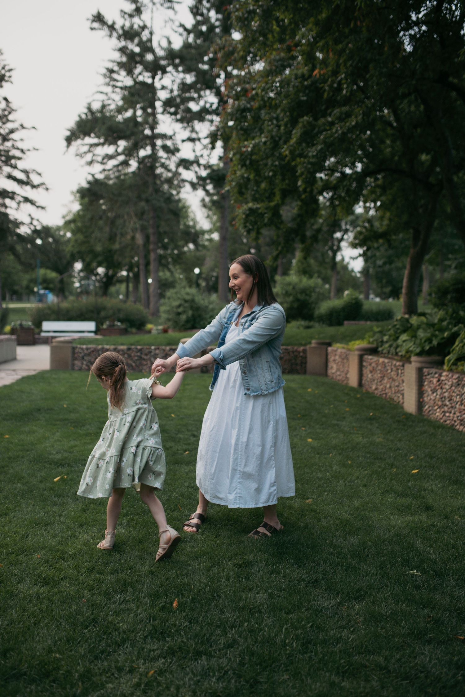 Joyful mother and daughter hold hands dancing on lush green park grass.
