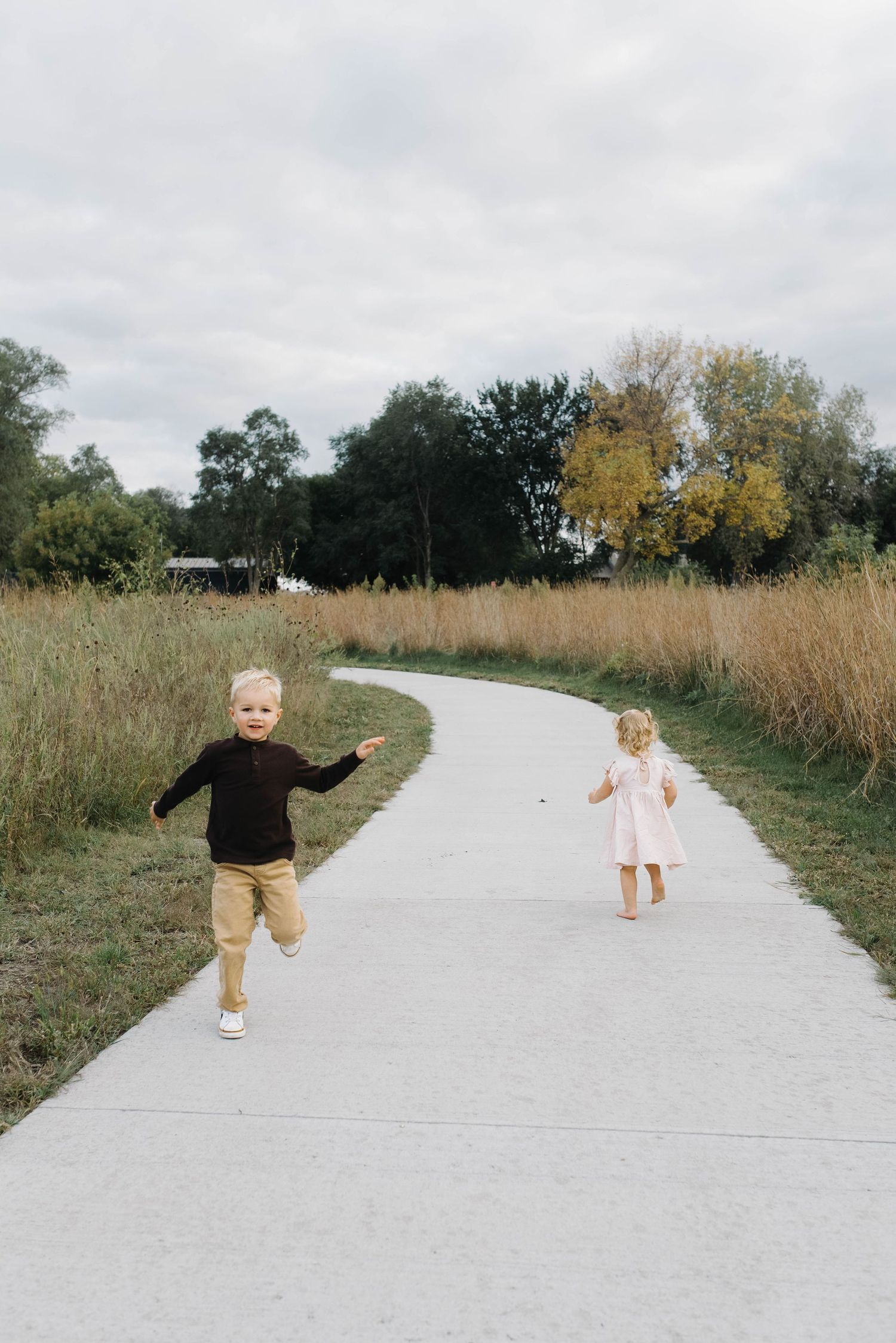 Two energetic young children running and playing on a winding path surrounded by tall autumn grass.