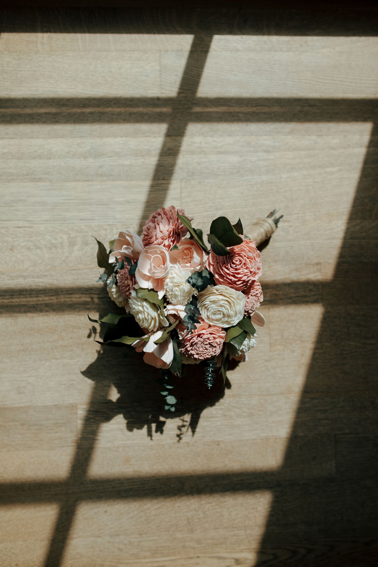 Elegant bridal bouquet with pink and blush flowers casting shadows on wooden floor.