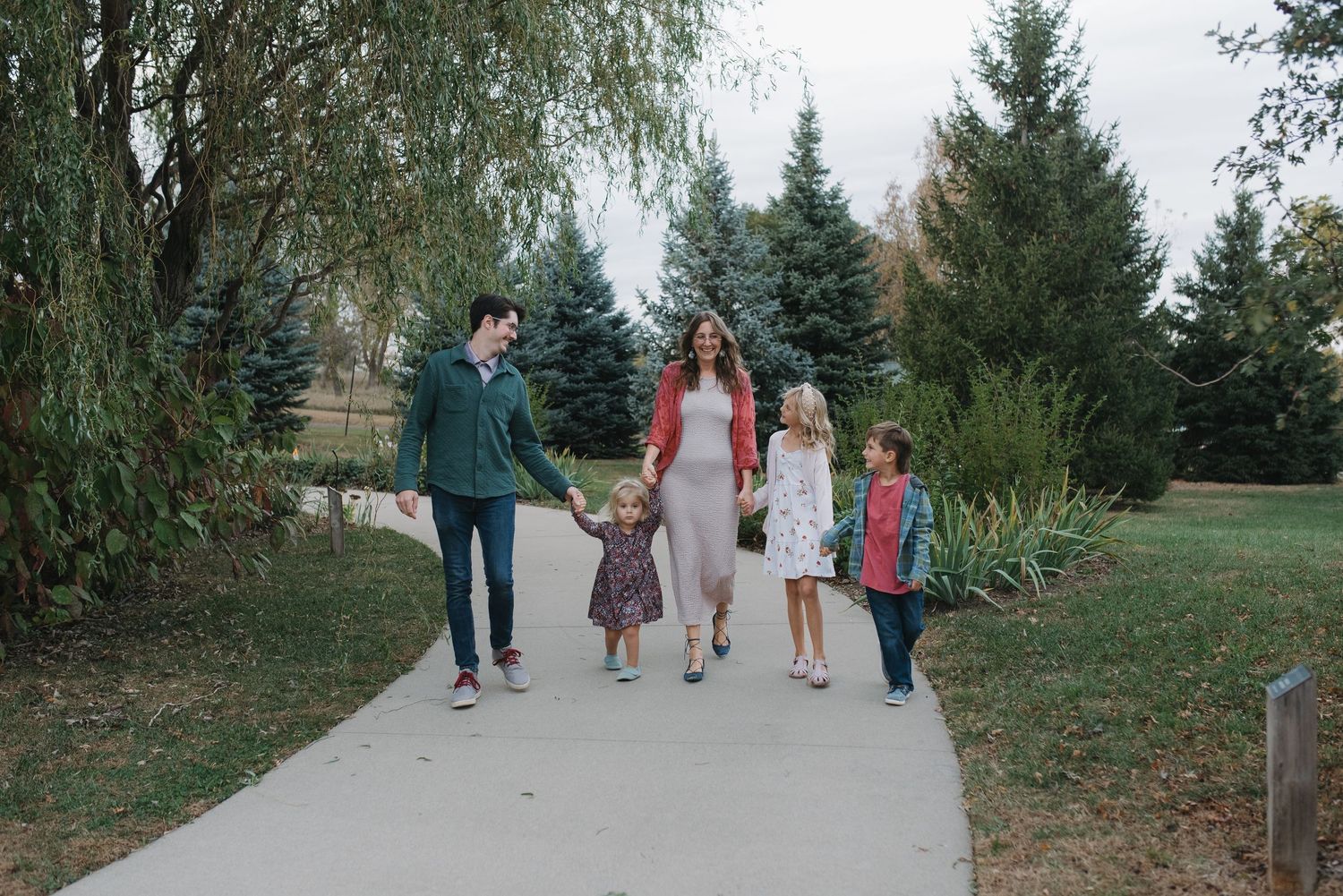 Family of five enjoying a walk on a park path with weeping willow nearby.