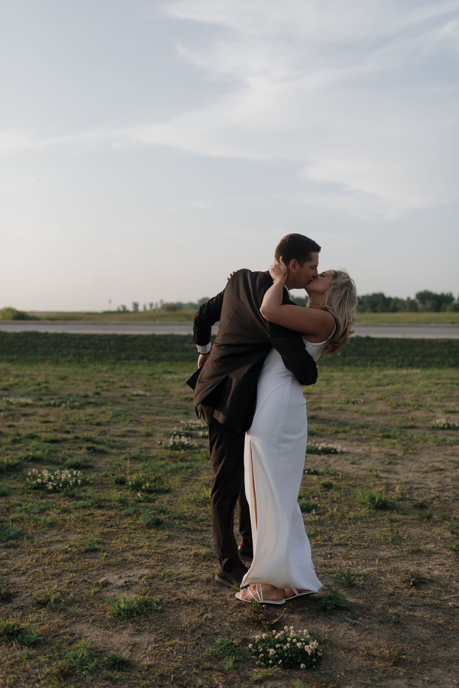 Couple shares a tender kiss in open field with groom lifting bride during wedding shoot.