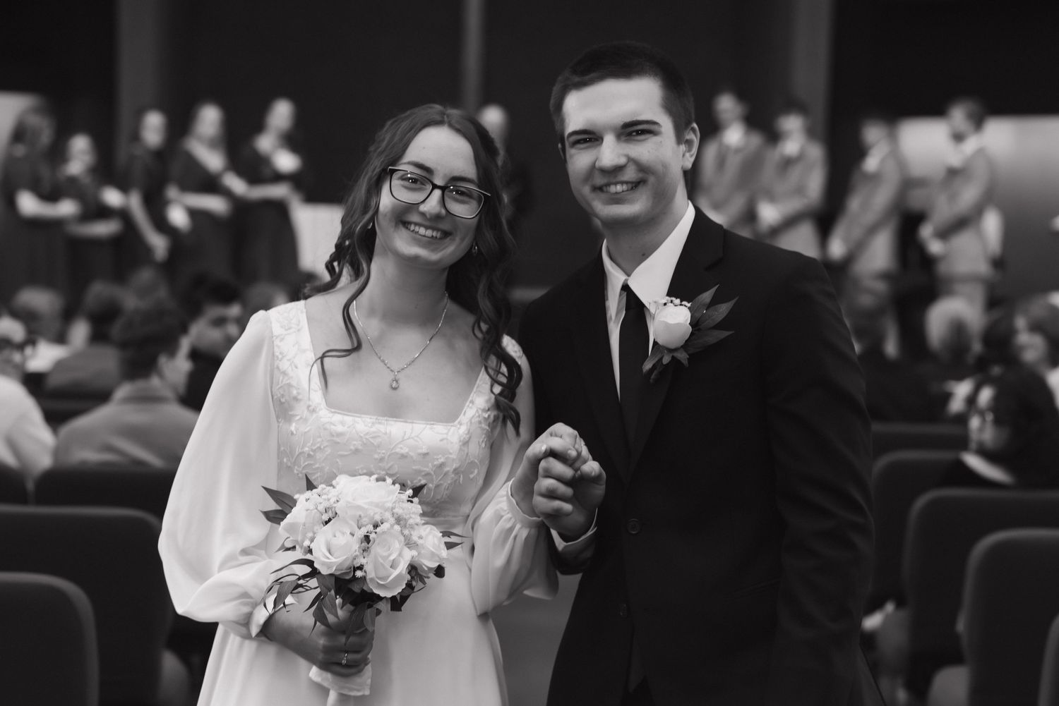 Black and white photo of smiling bride and groom holding hands after wedding ceremony.