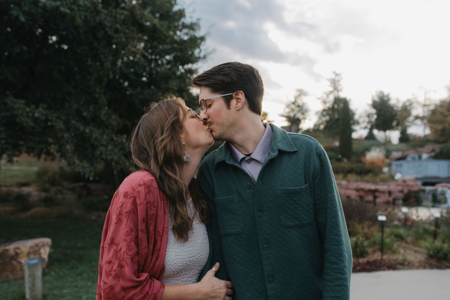A couple shares a tender kiss outdoors in a garden with soft evening light.