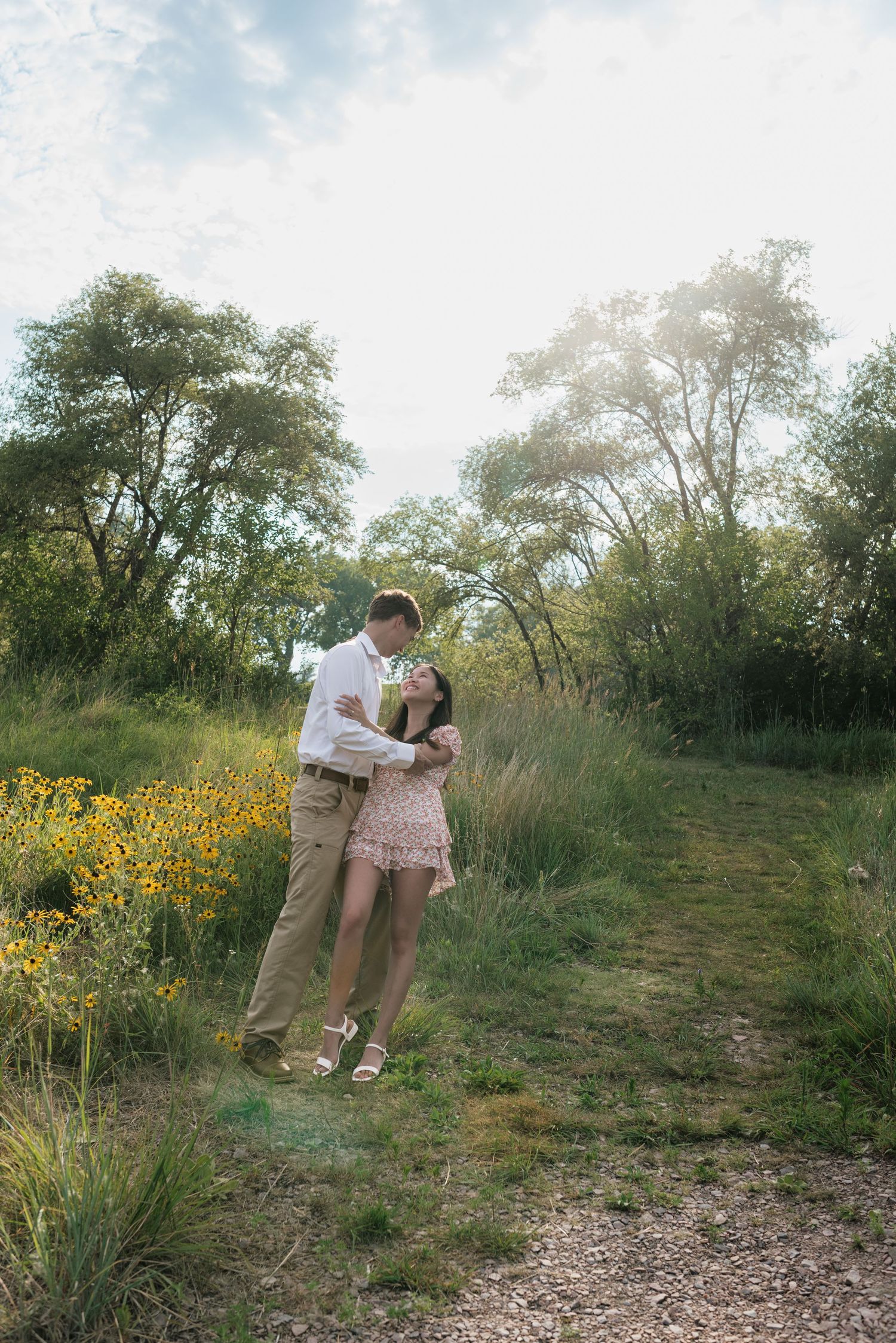 Young couple sharing a romantic moment on a sunlit nature trail surrounded by lush greenery and wildflowers.
