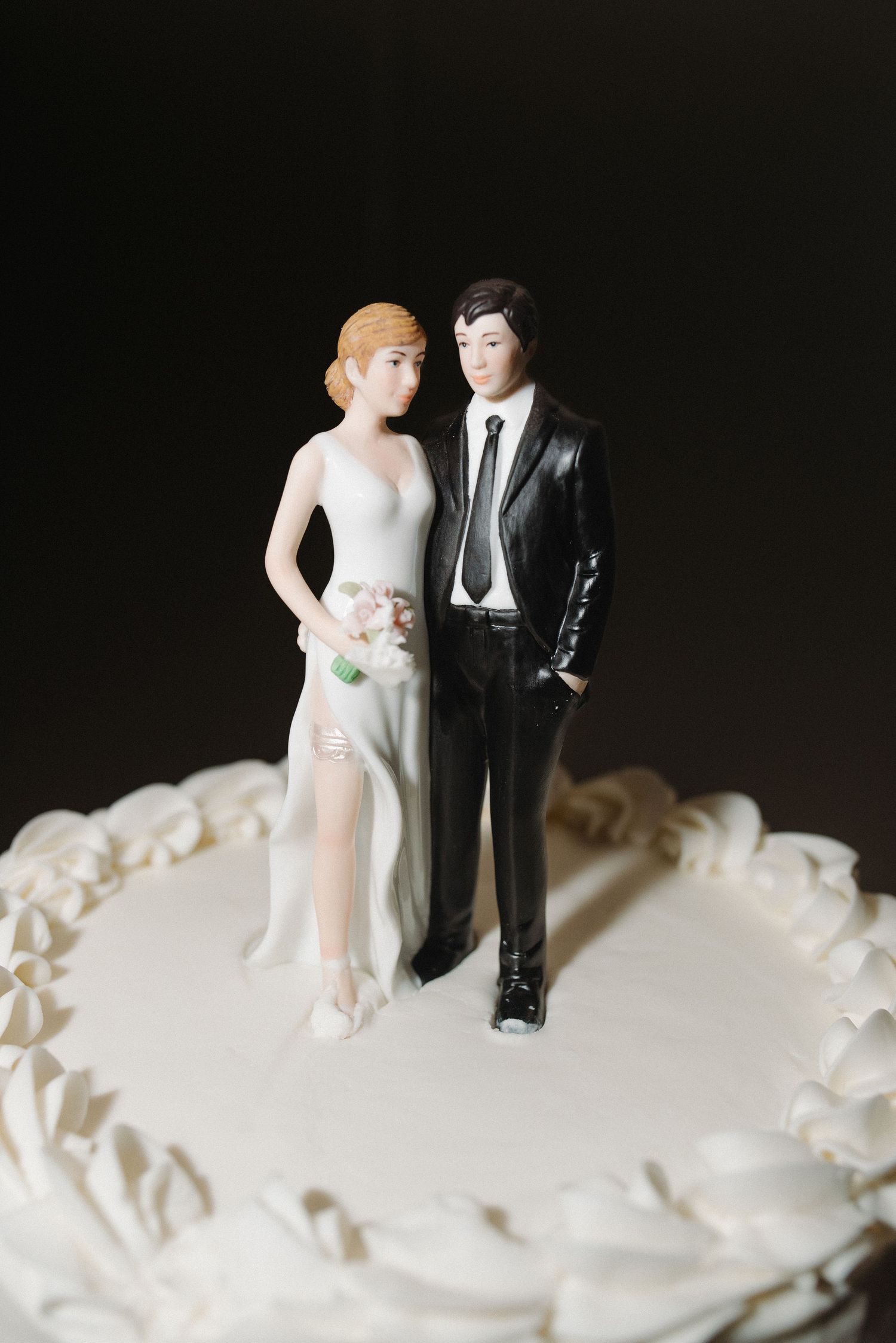 Close-up of vintage-style ceramic bride and groom cake topper on white frosted wedding cake.