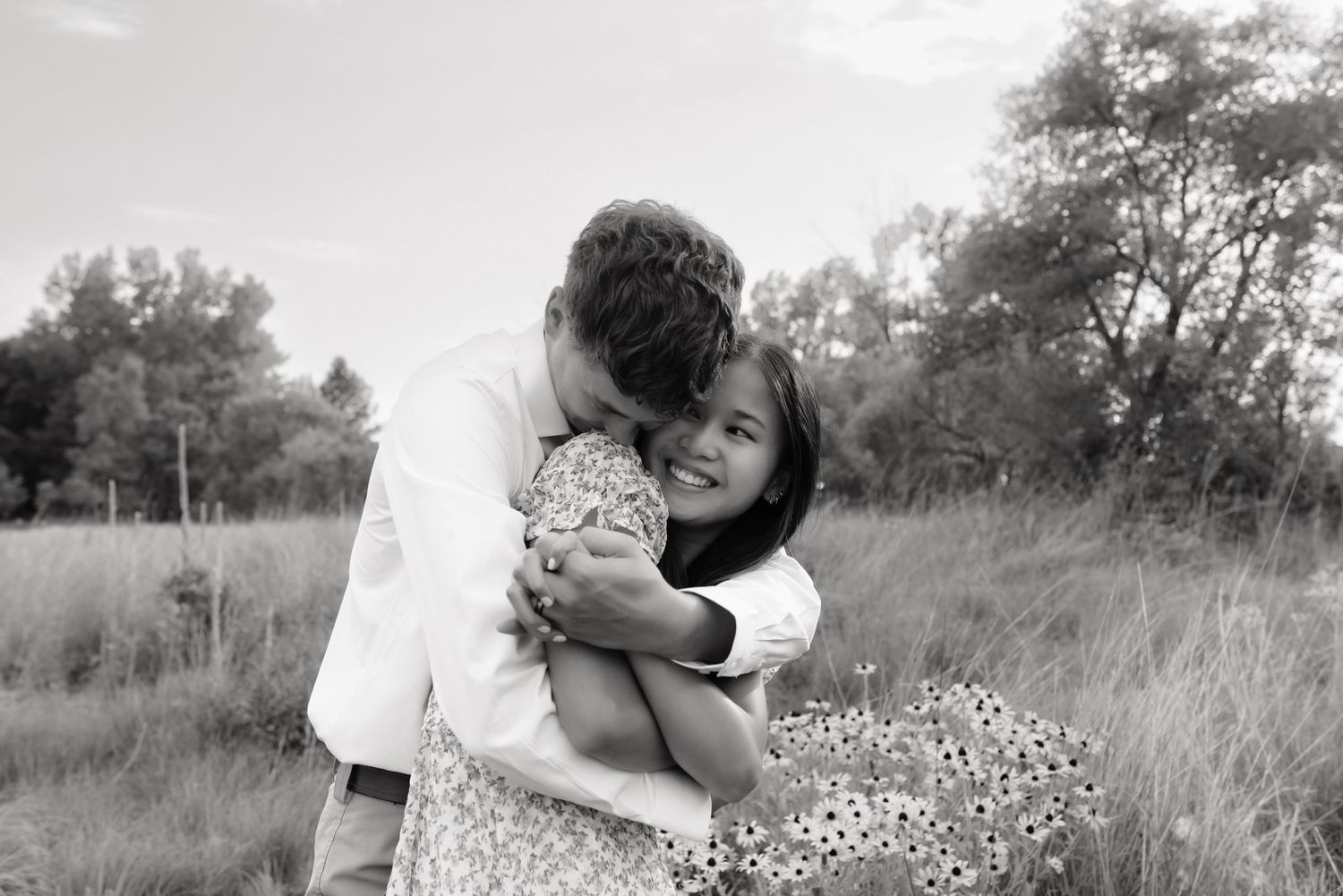 Black and white photo of a couple embracing and laughing in a grassy field.