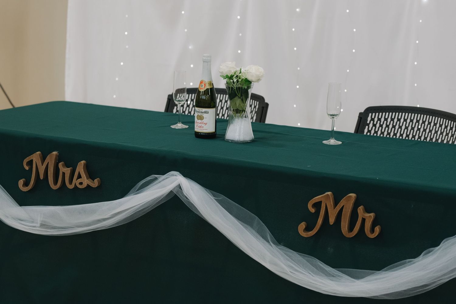 Elegant green sweetheart table decorated with Mr and Mrs signs, white tulle, and floral centerpiece.
