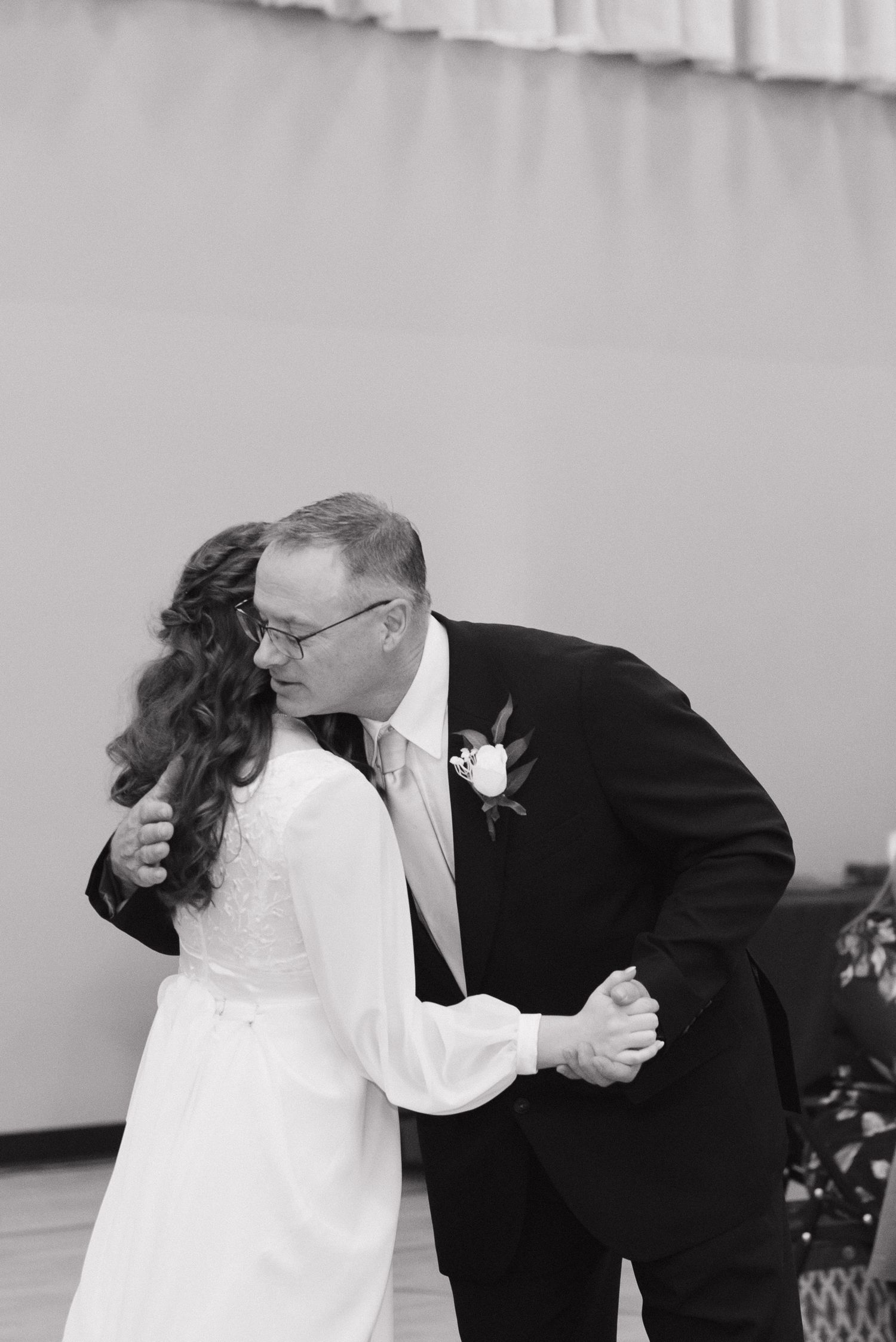 Black and white photo of a bride and father sharing an emotional first dance at a wedding reception.