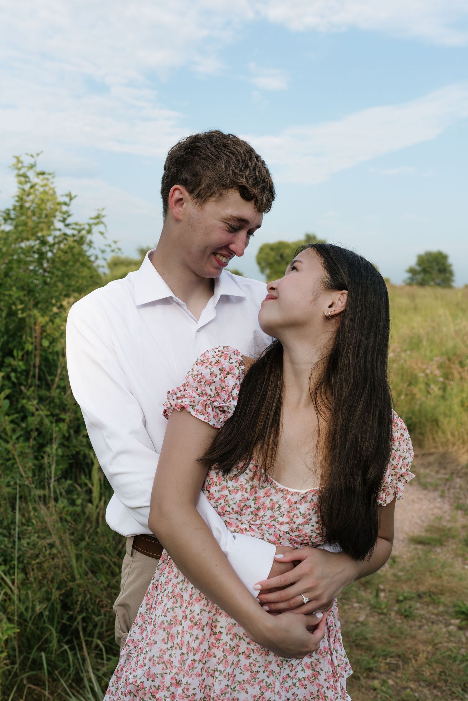 Smiling couple embracing outdoors in a green field under a blue sky.