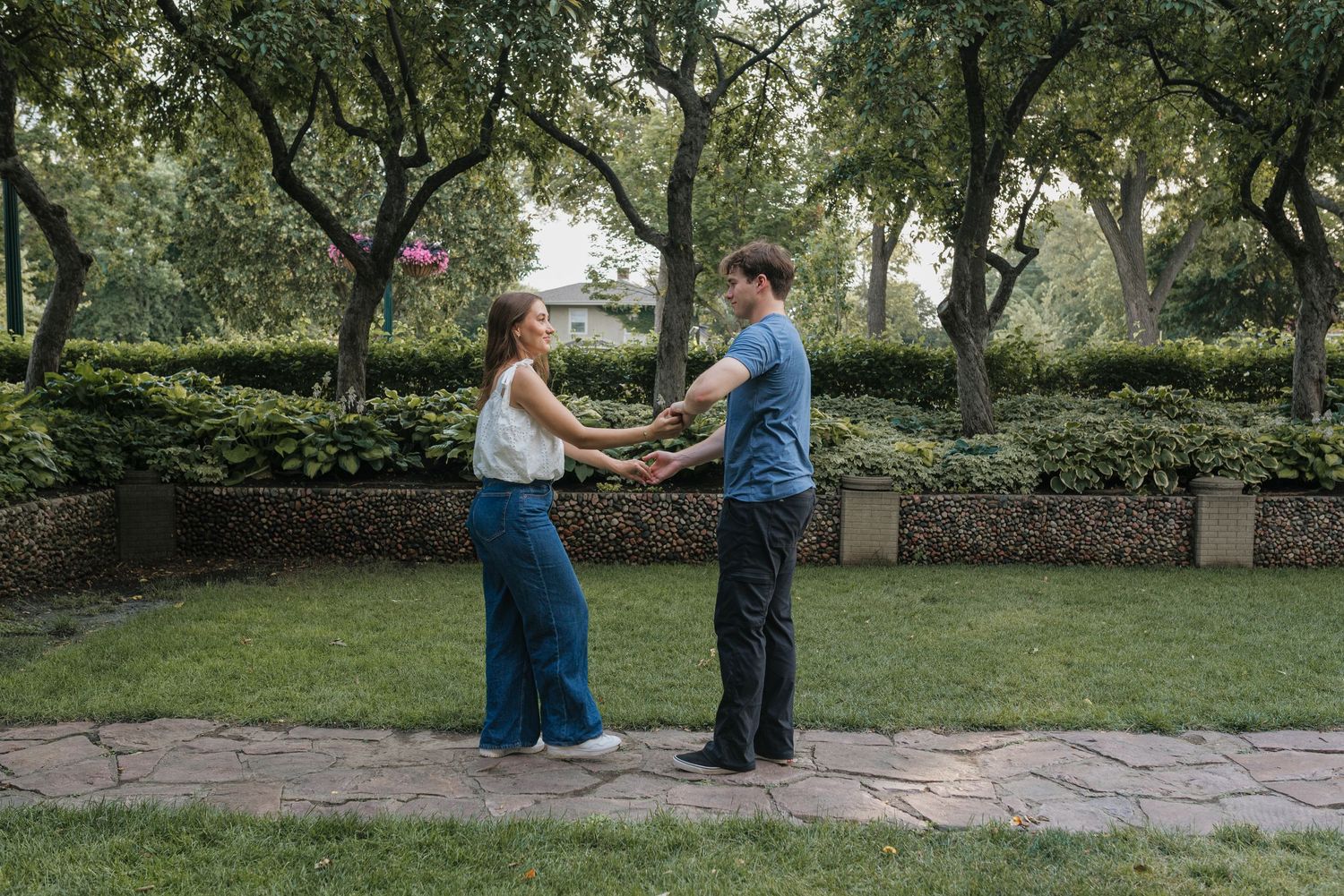 Couple holding hands and playing with a frisbee in a lush green park surrounded by trees.