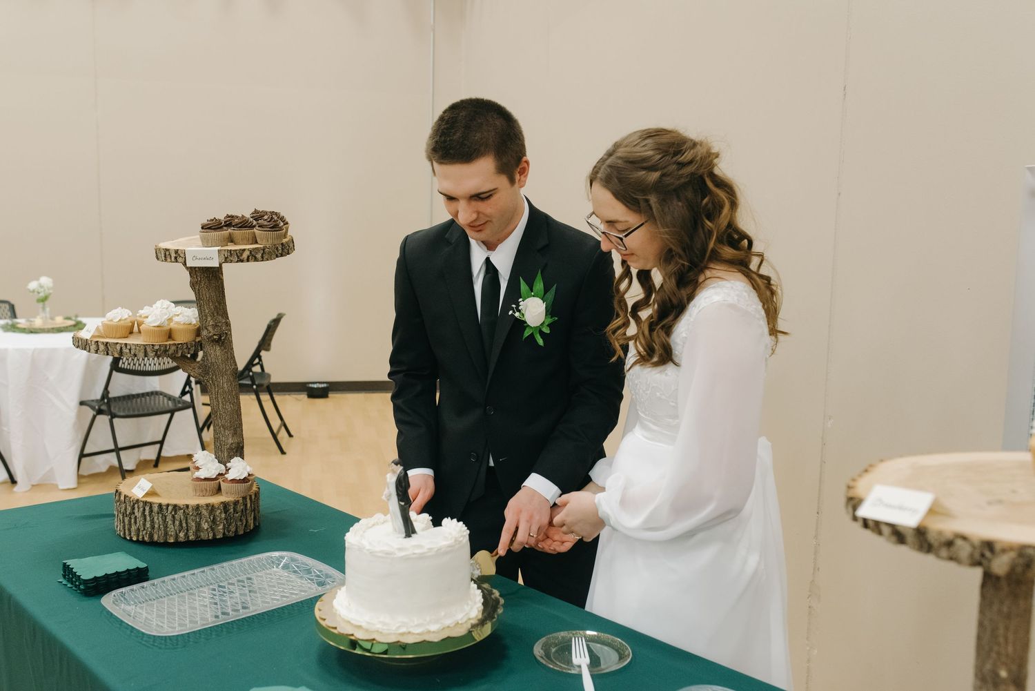 Bride and groom cutting their white wedding cake together at a reception table with a green tablecloth.