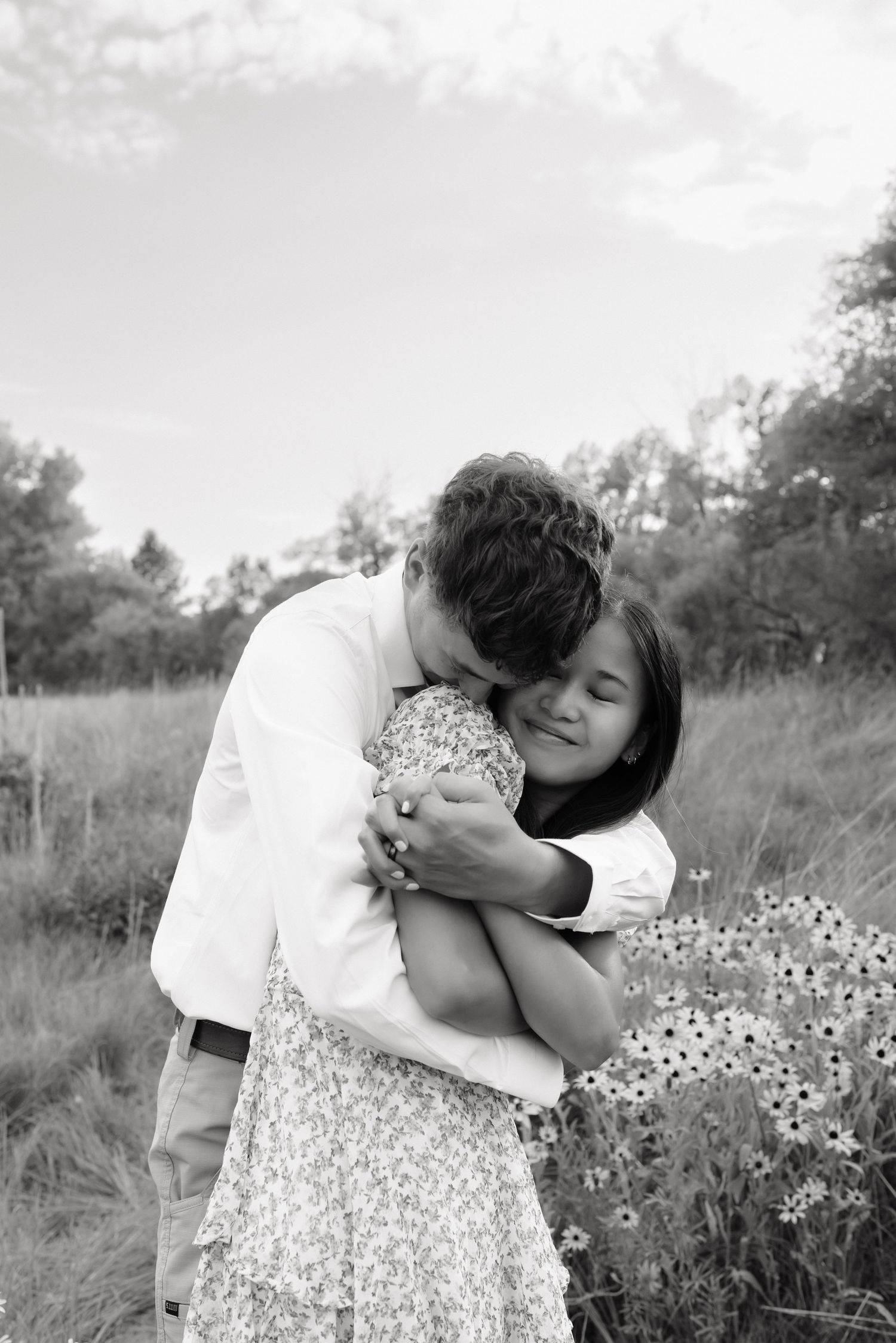 Black and white photo of a couple sharing a warm embrace in a field of wildflowers.