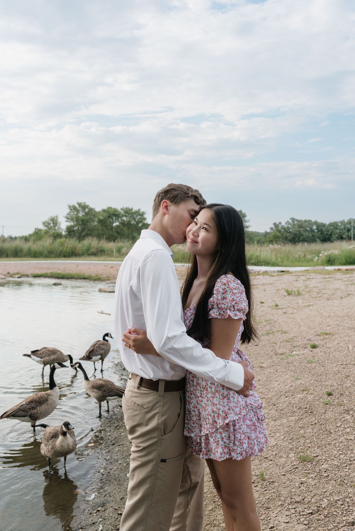 Romantic couple standing close near a lakeside with Canada geese wading in the water.