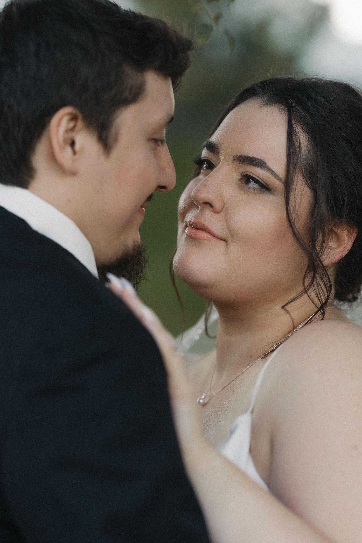 Intimate wedding portrait of bride gazing lovingly at groom in soft outdoor light.