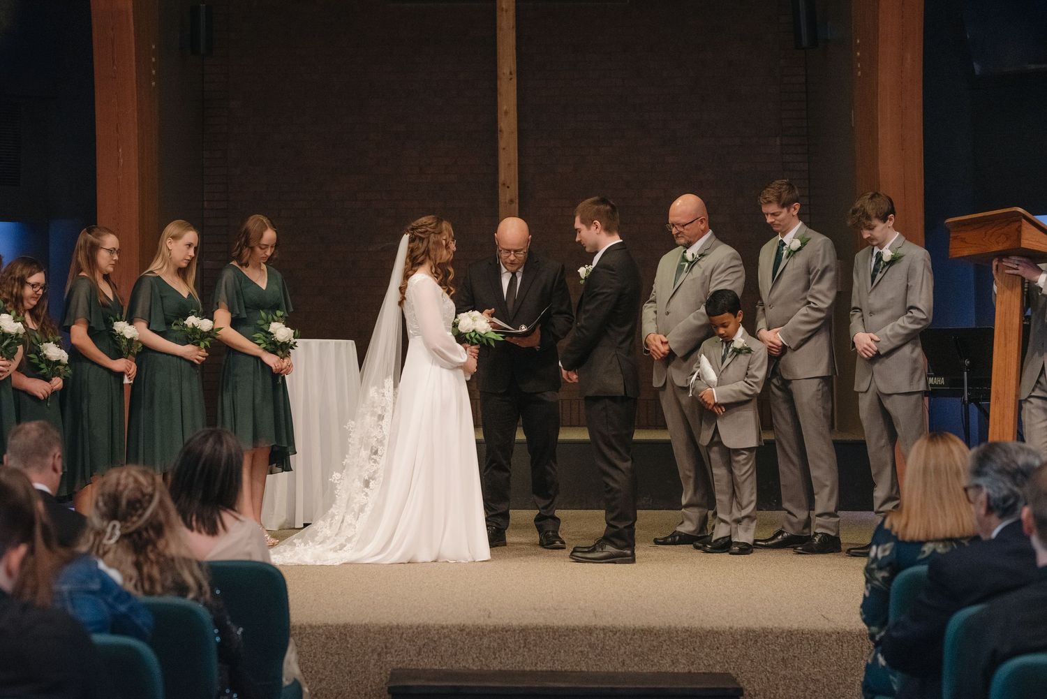 Bride and groom exchange vows at the altar surrounded by bridesmaids and groomsmen.