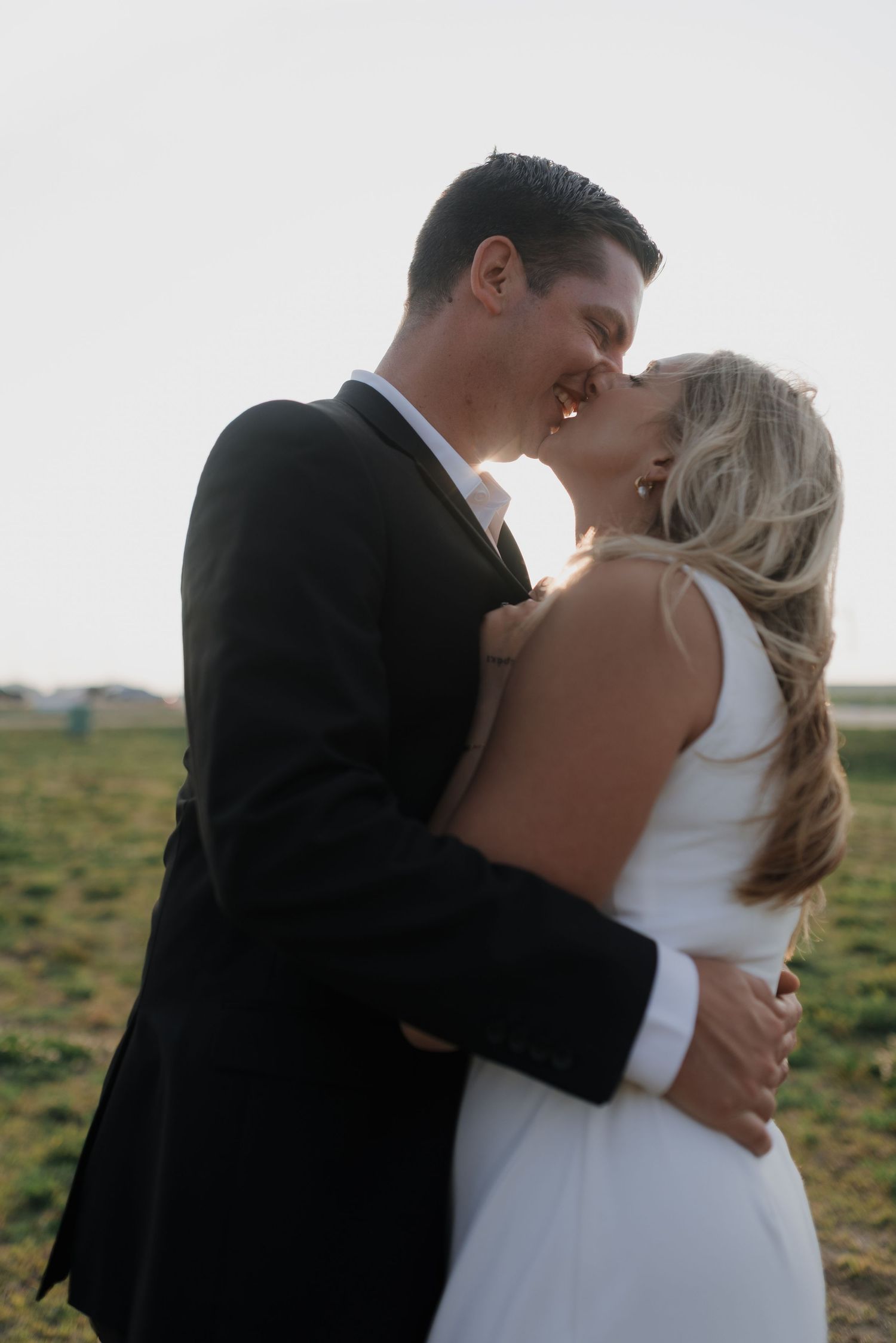 Bride and groom sharing a tender kiss outdoors with soft golden hour light in the background.