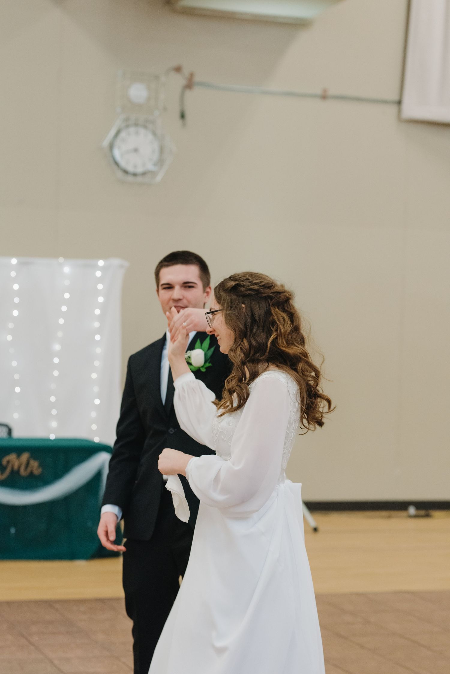 Bride in white long-sleeve gown kisses groom's hand during first dance at elegant wedding reception.